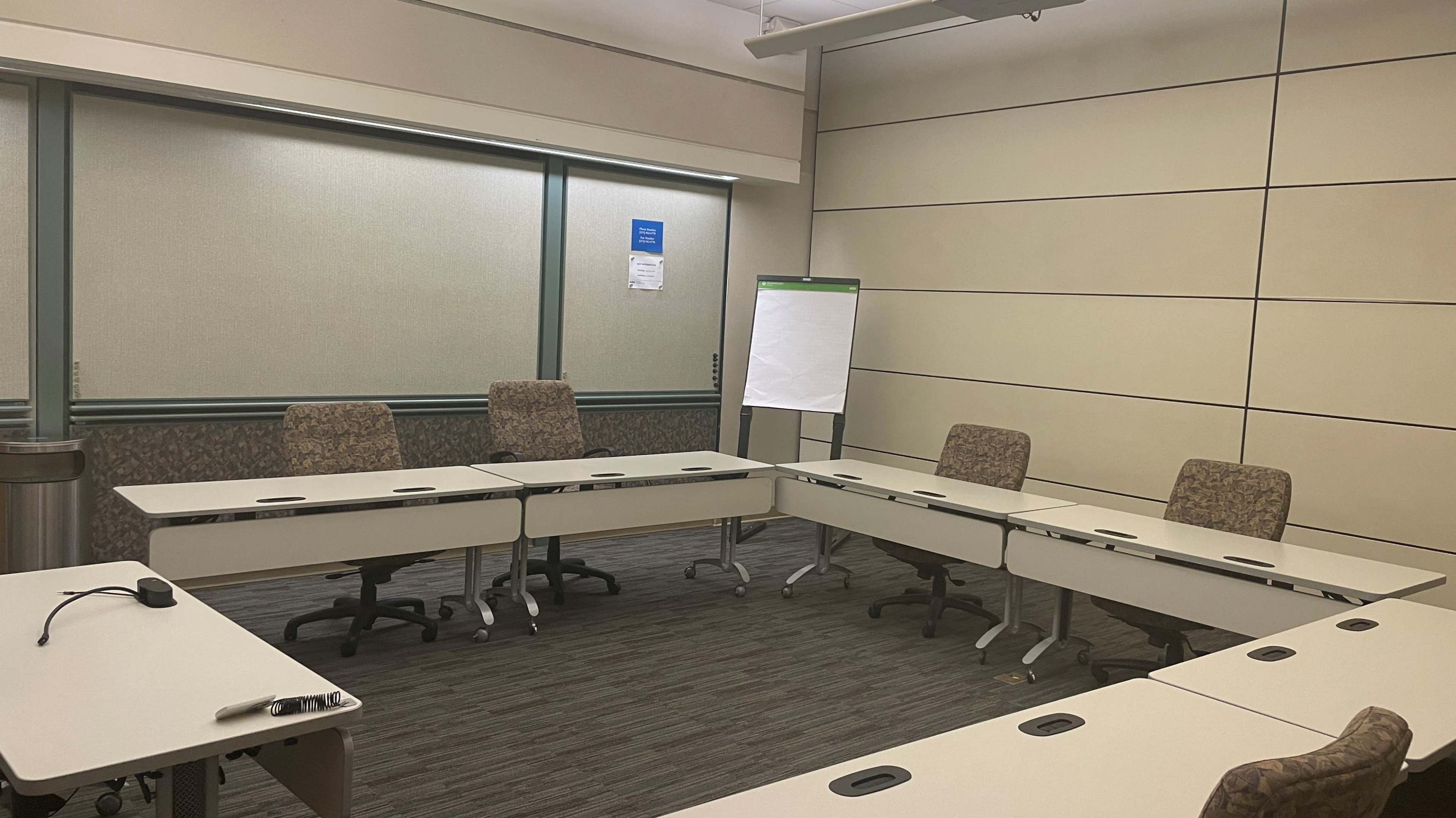 A conference room is arranged with several tables and chairs in a circular layout, featuring a flip chart at one end.