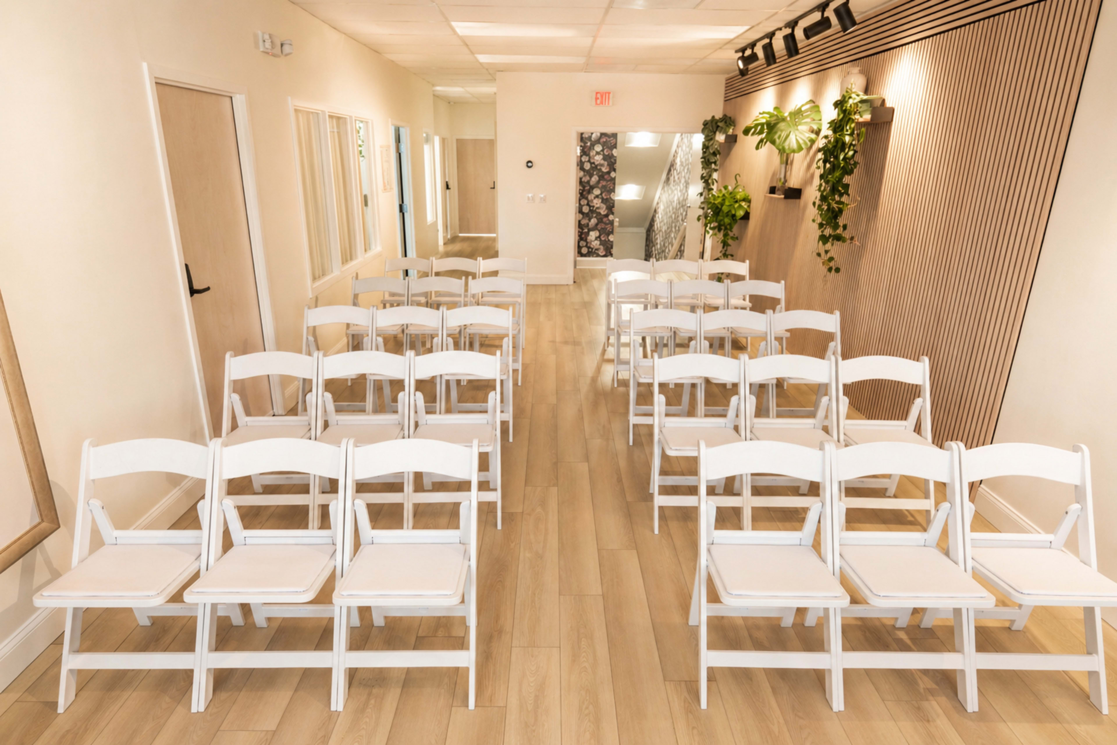 The image shows a well-lit indoor space set up with rows of white folding chairs on a wooden floor.