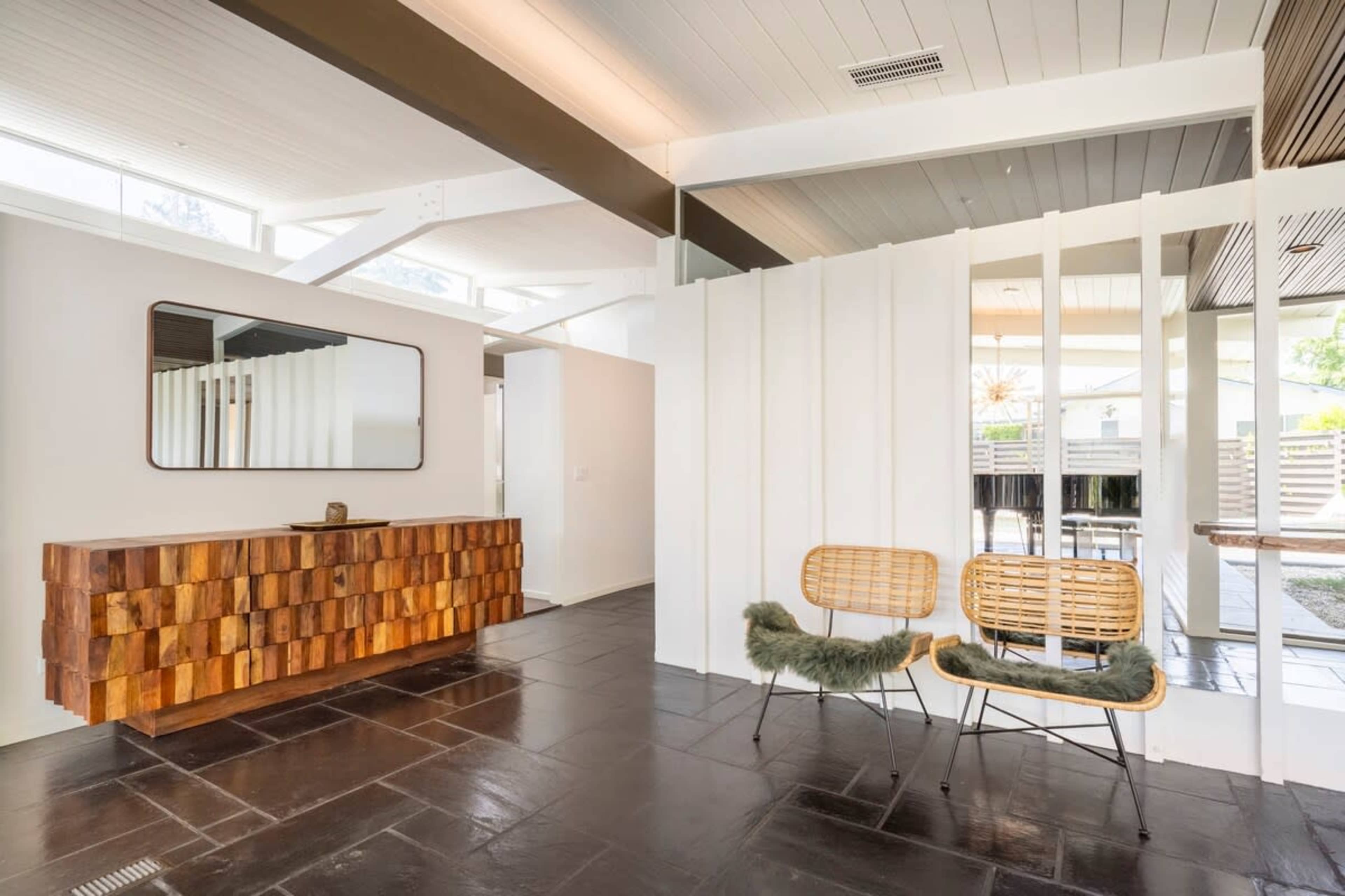 The image depicts a modern interior space featuring a wooden console table, two woven chairs, and partitions separating areas within the room.
