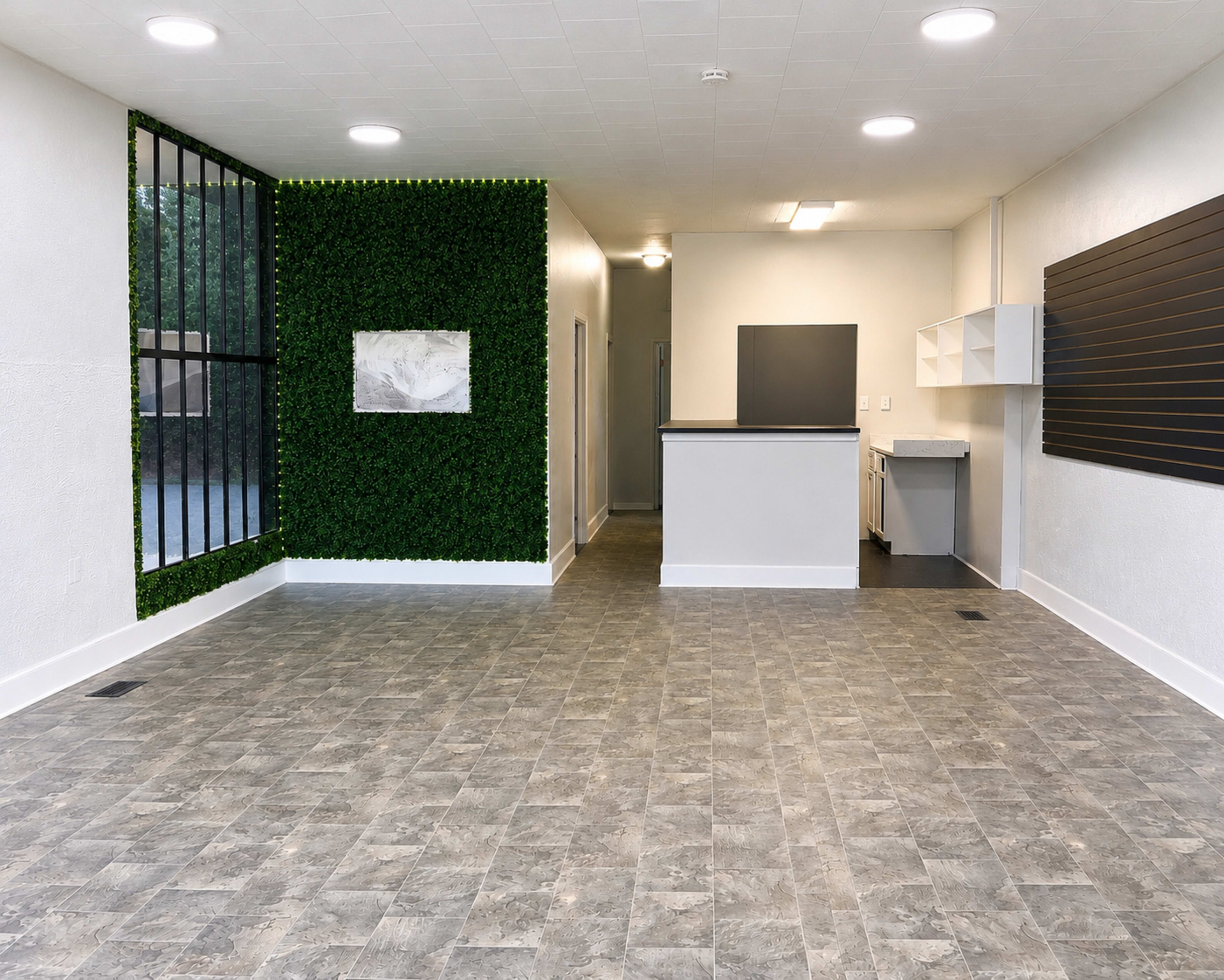 The image shows a spacious interior with a green plant wall, light-colored walls, and modern flooring, featuring a kitchen area to the right.