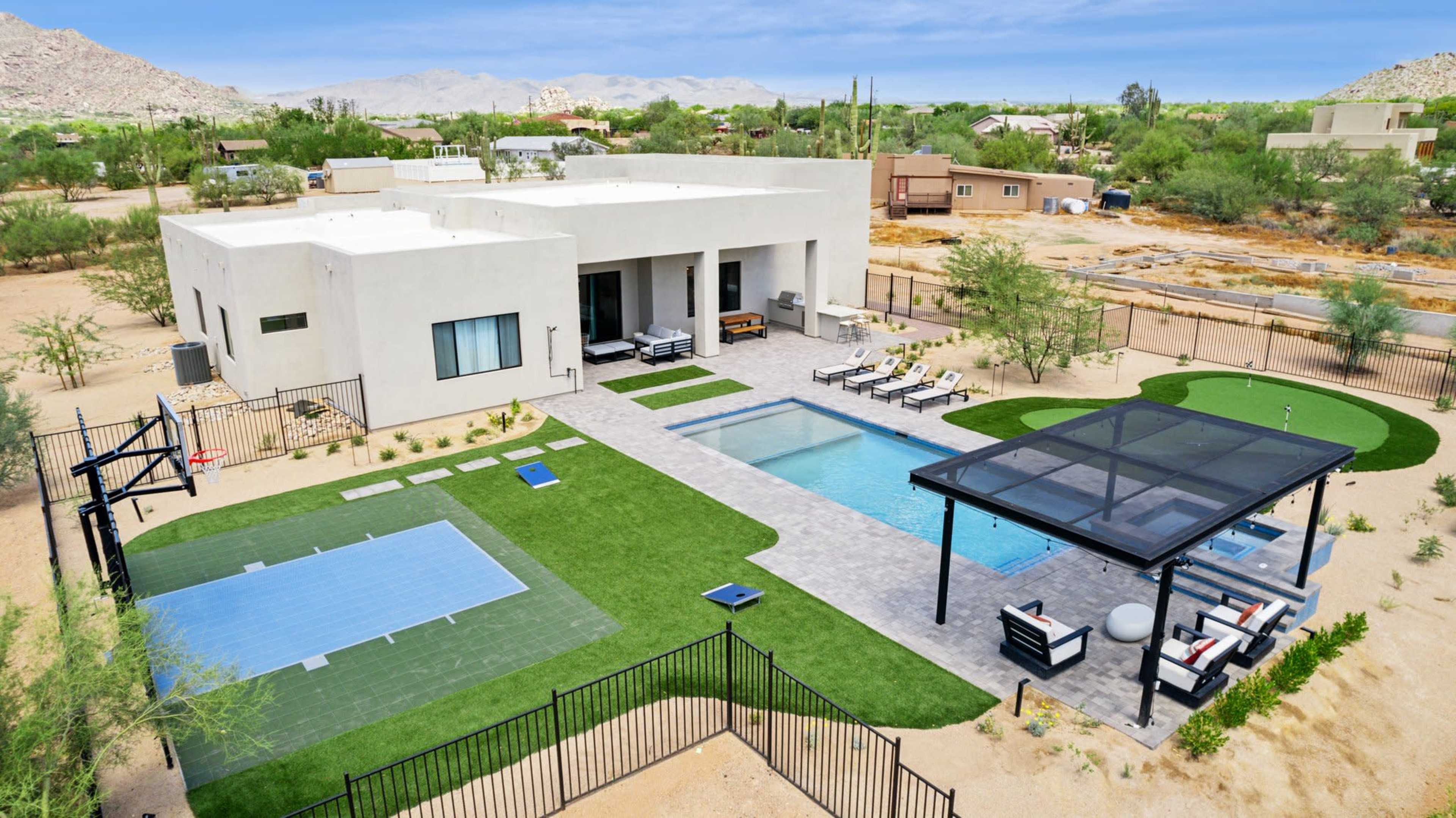 The image shows a modern house with a swimming pool, surrounded by a landscaped yard featuring artificial grass and sports areas.