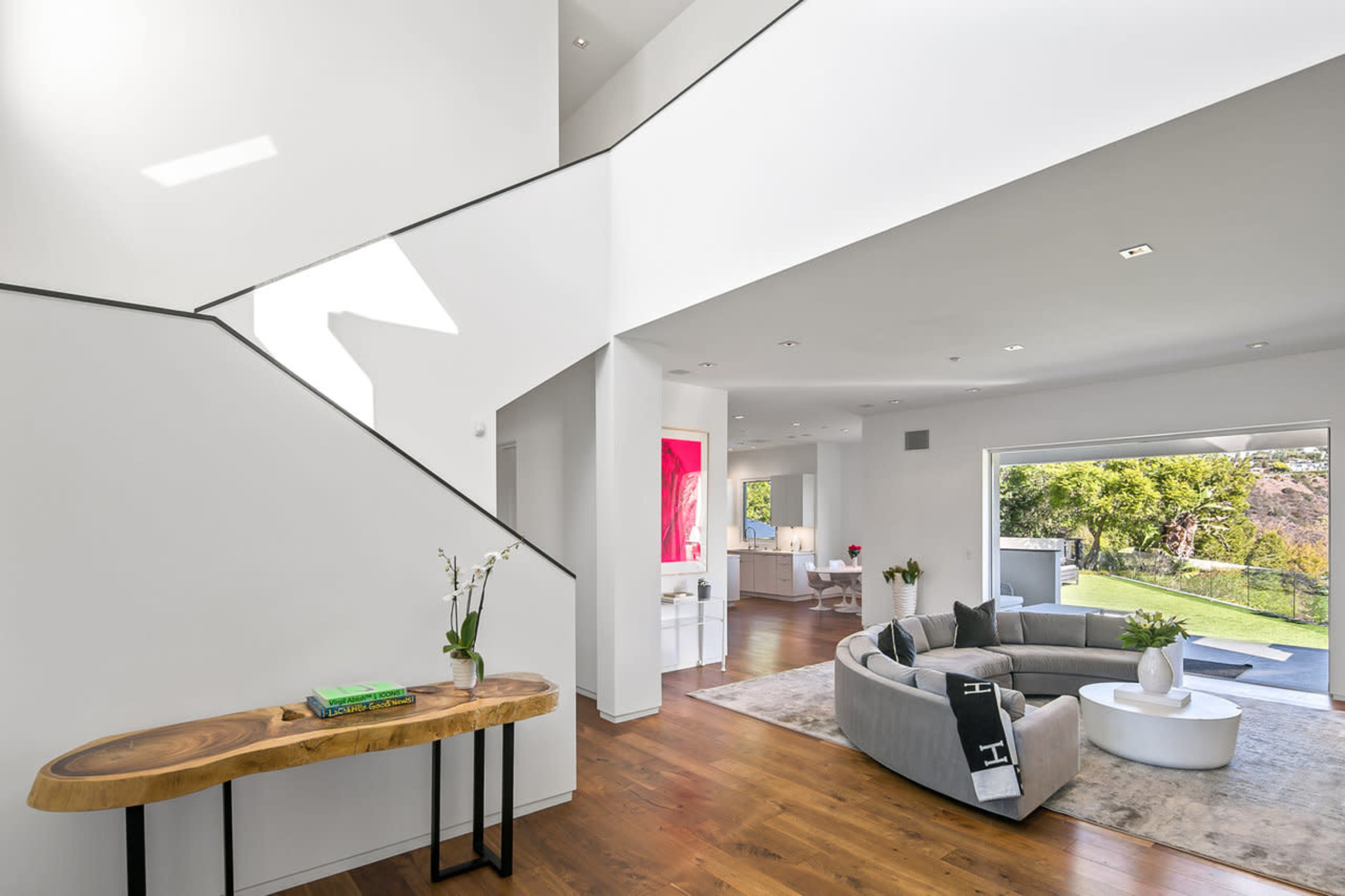 A modern interior with a staircase, a curved gray sofa, and large windows leading to a landscaped outdoor area.