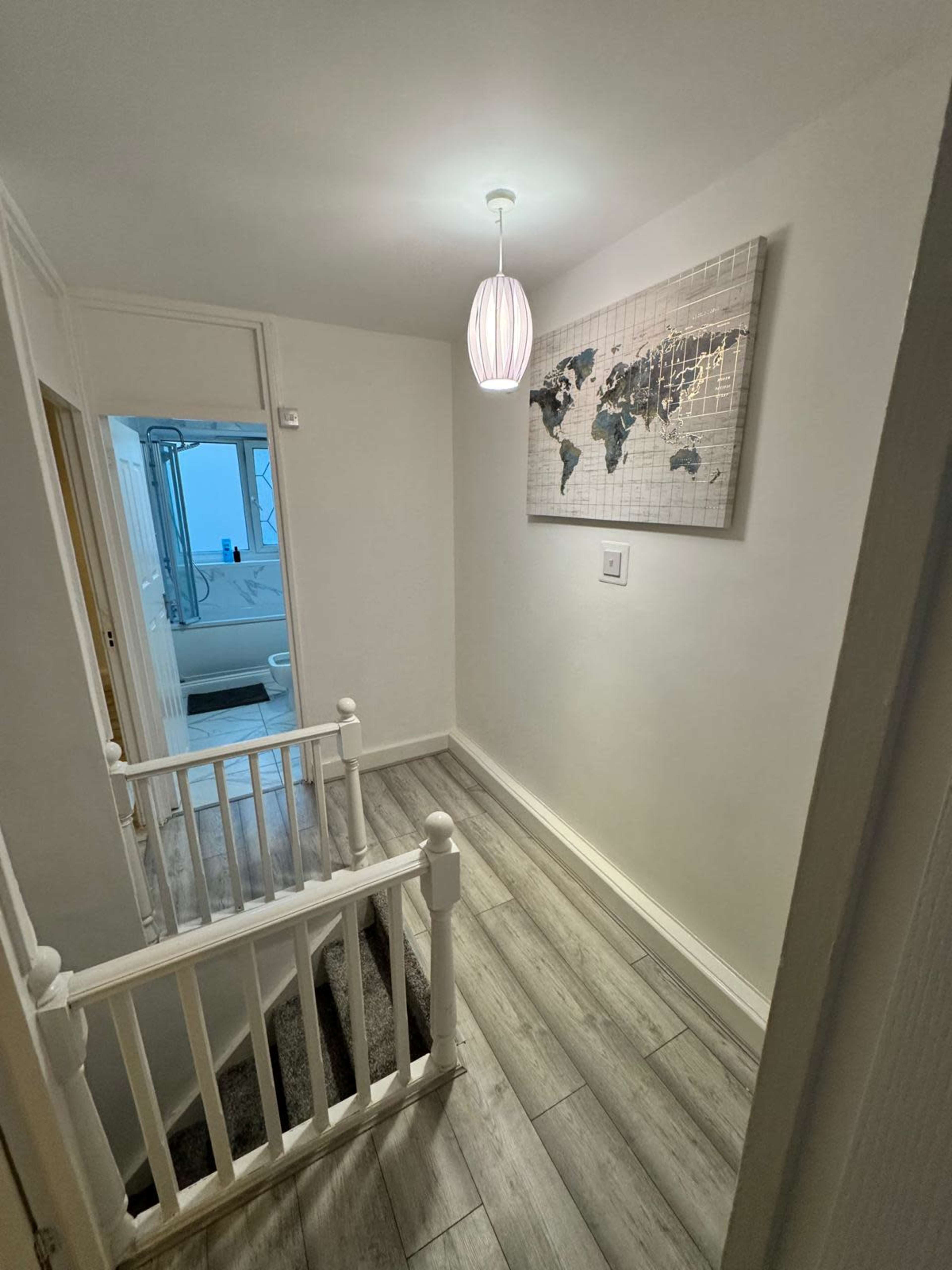 The image shows a hallway with white walls, a decorative world map on the wall, and a light fixture hanging from the ceiling.