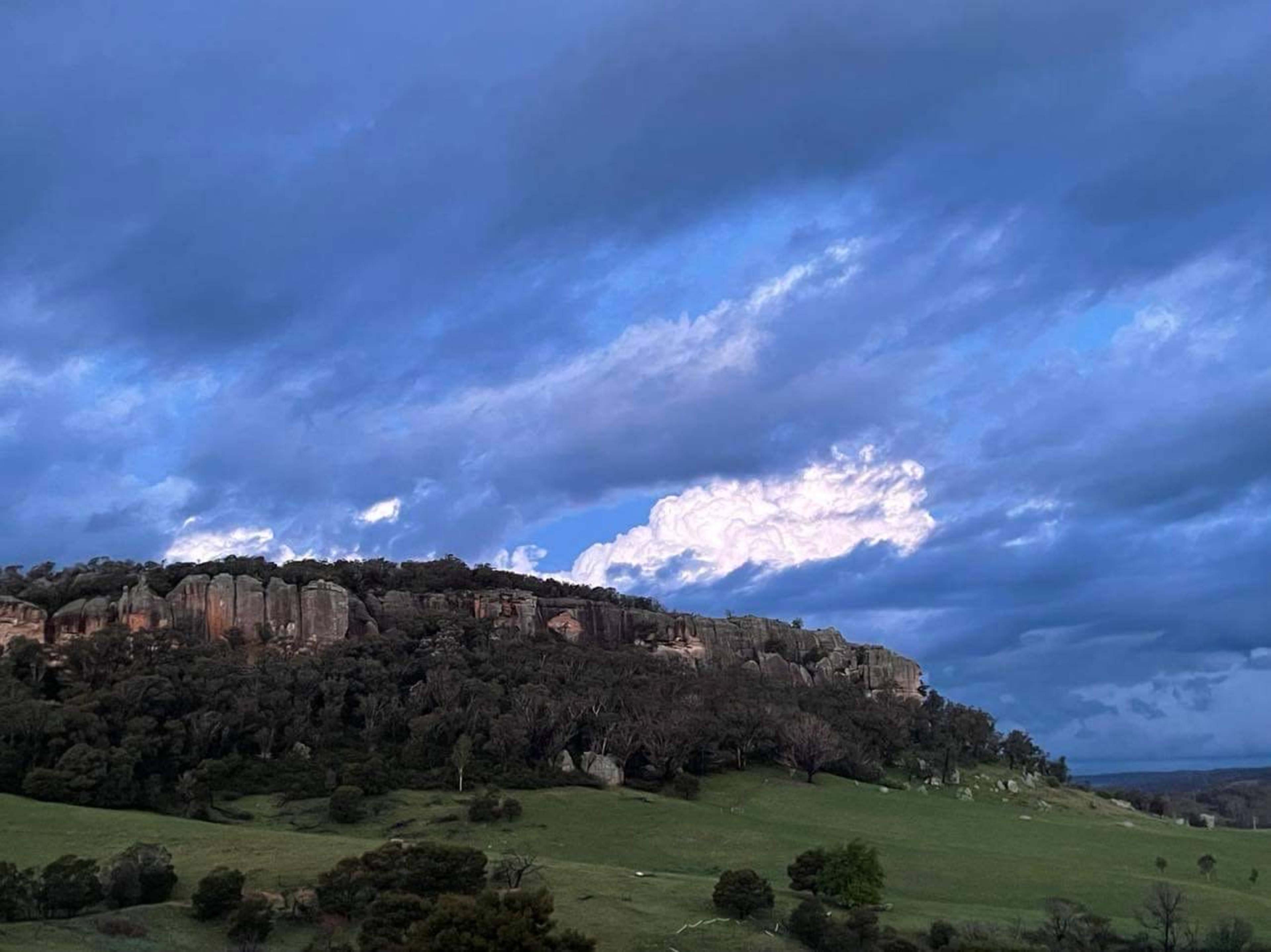 A rocky outcrop rises against a cloudy sky above a green landscape.