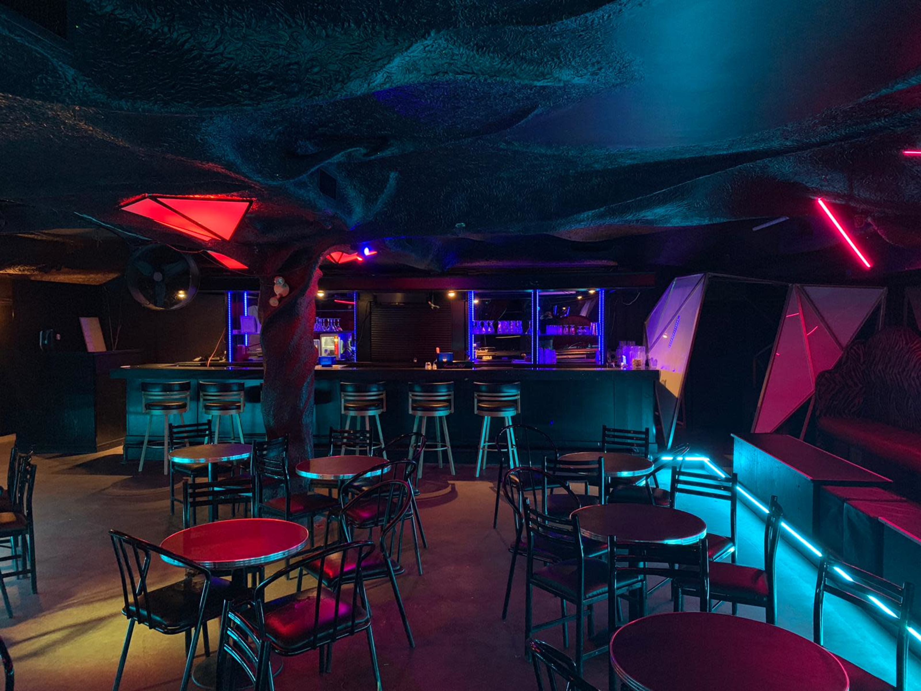 A person adjusts the lighting in a modern bar that features a unique ceiling design and colorful LED lights amidst rows of empty tables and chairs.
