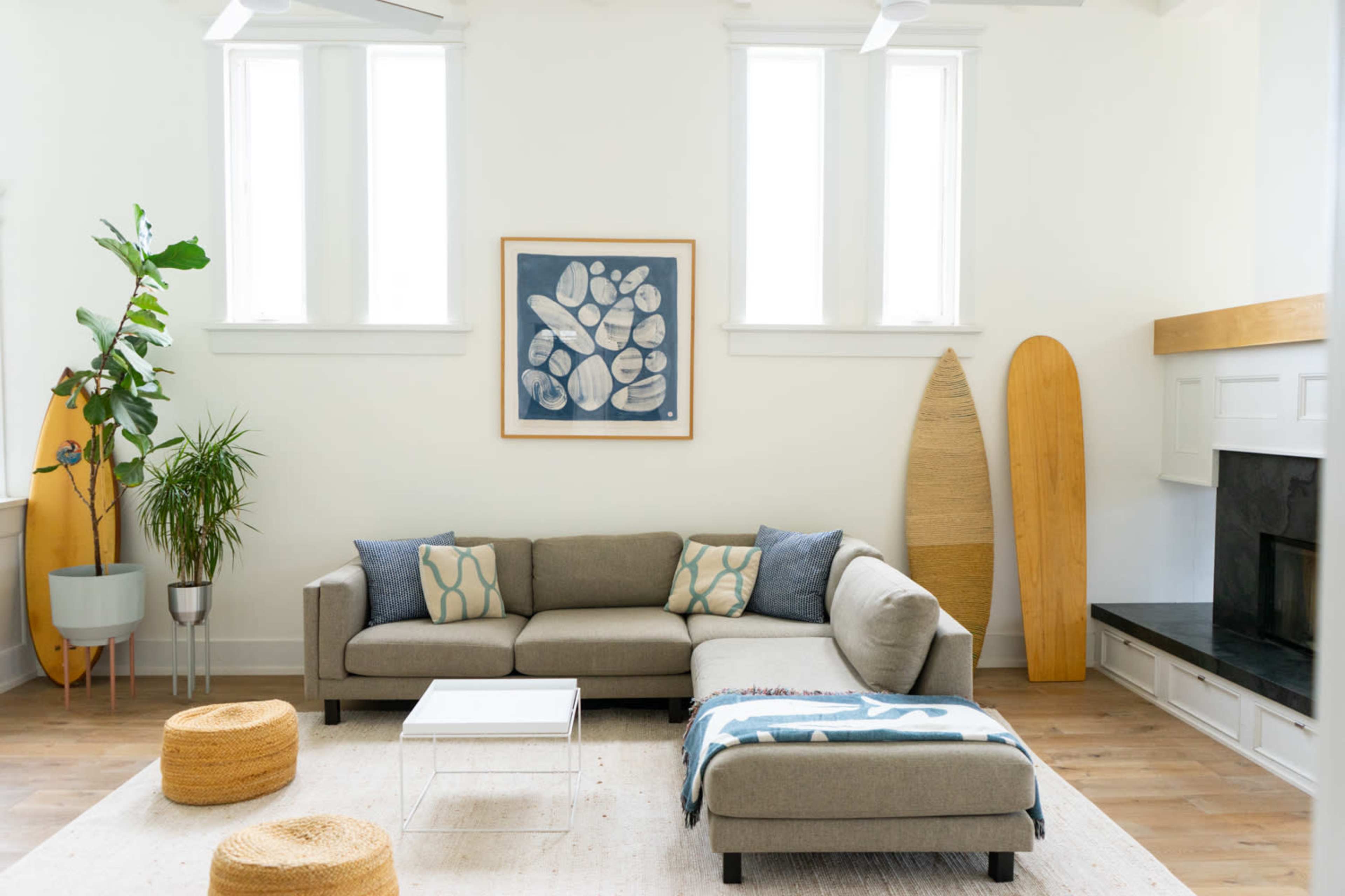 A modern living room featuring a sectional sofa, two round stools, a fireplace, and surfboards leaning against the wall.