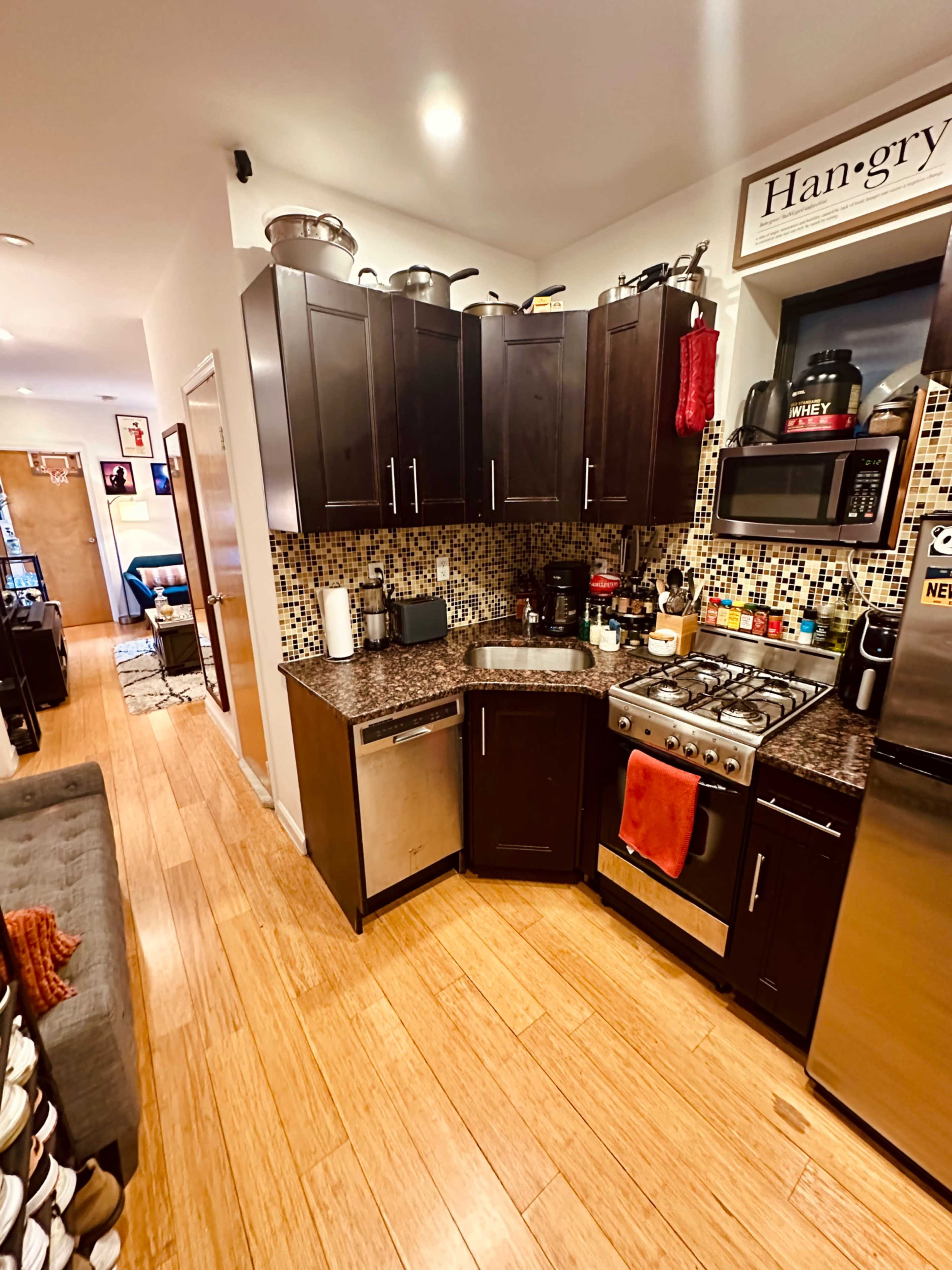 A compact kitchen with dark wooden cabinets, a stainless steel stove, and a mosaic tiled backsplash.