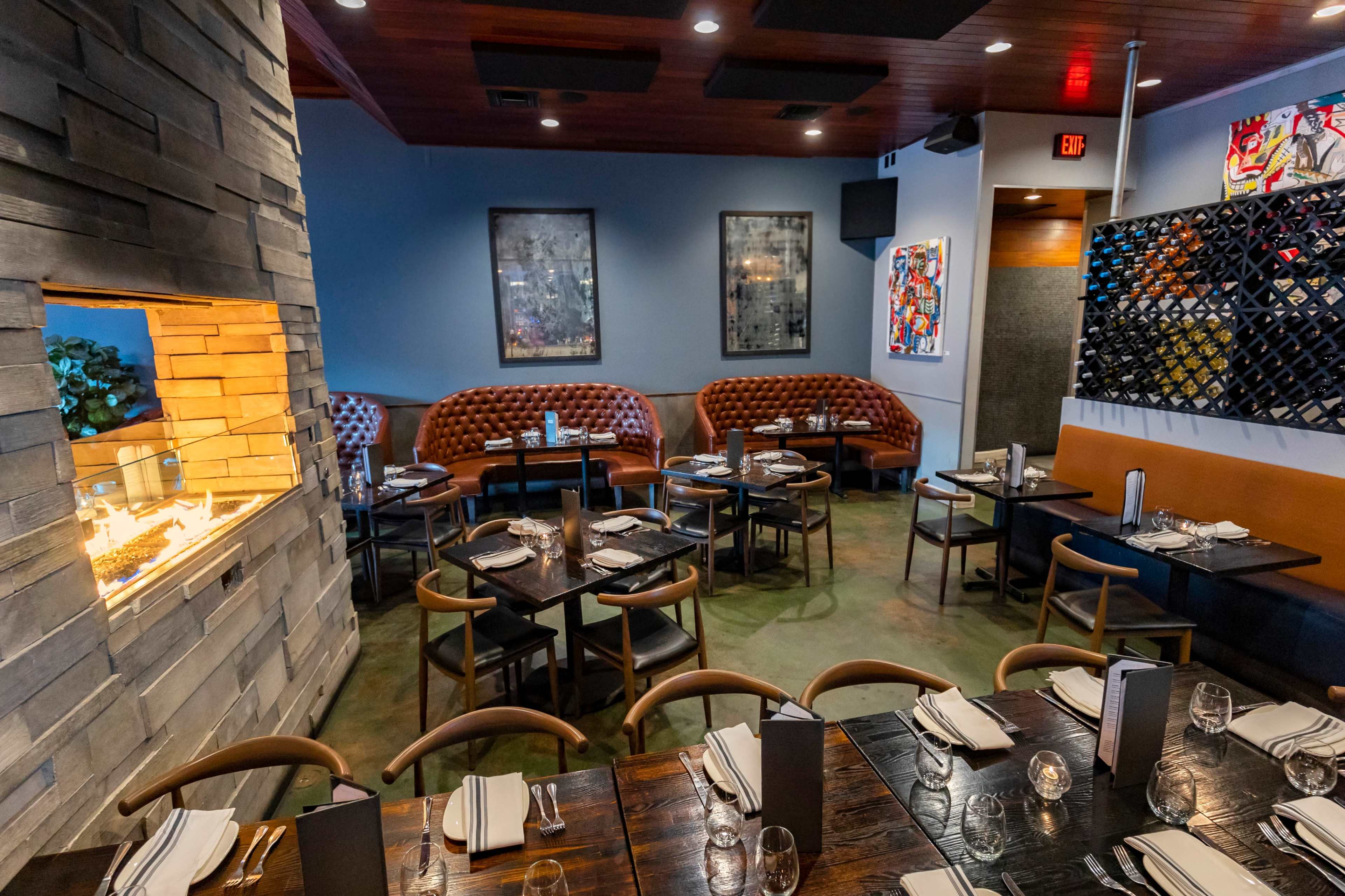 A modern restaurant interior featuring upholstered booths, a stone fireplace, and tables set for dining.
