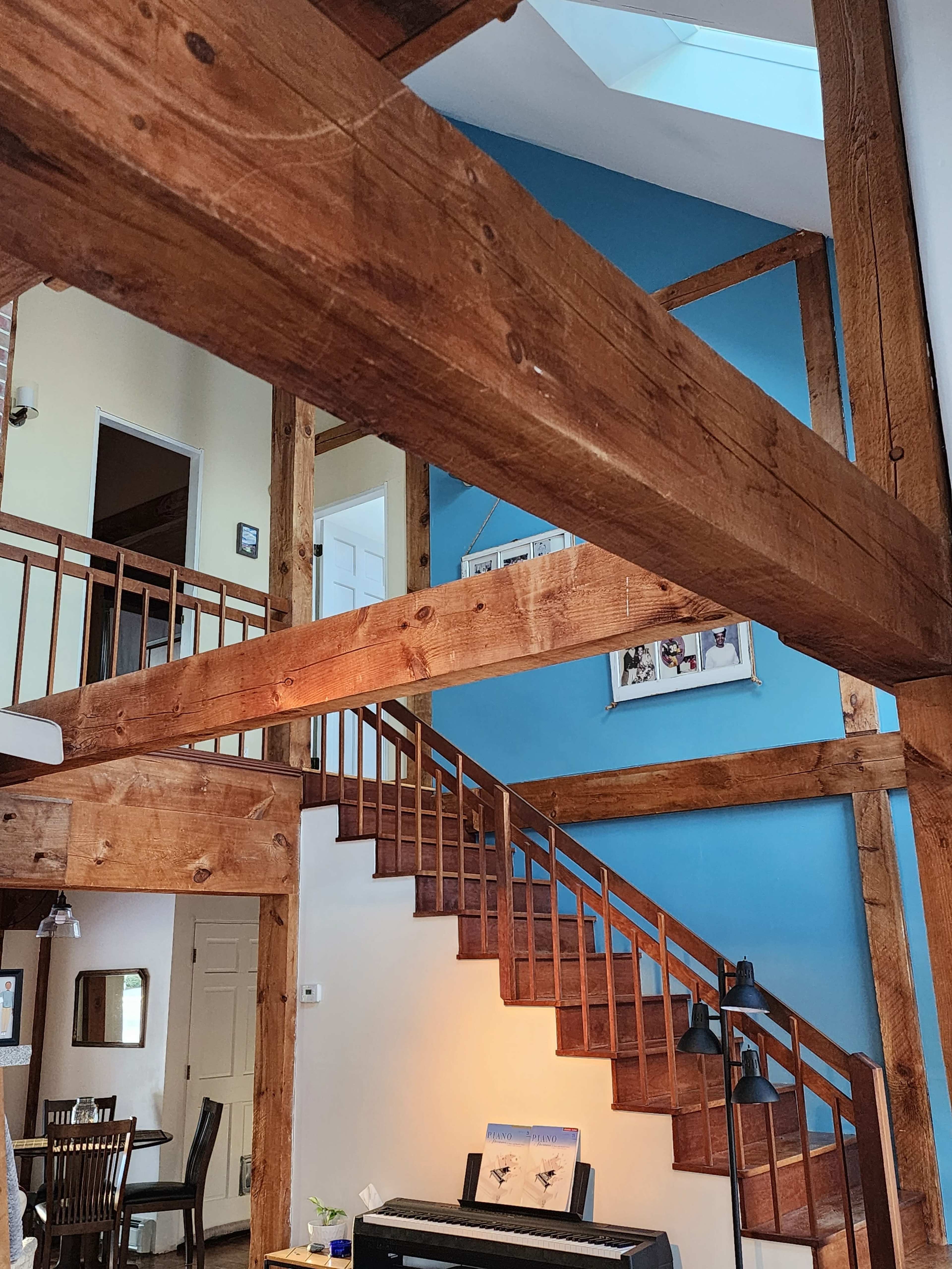 The image shows a wooden staircase leading to an upper level, surrounded by exposed wooden beams and walls painted in light colors.