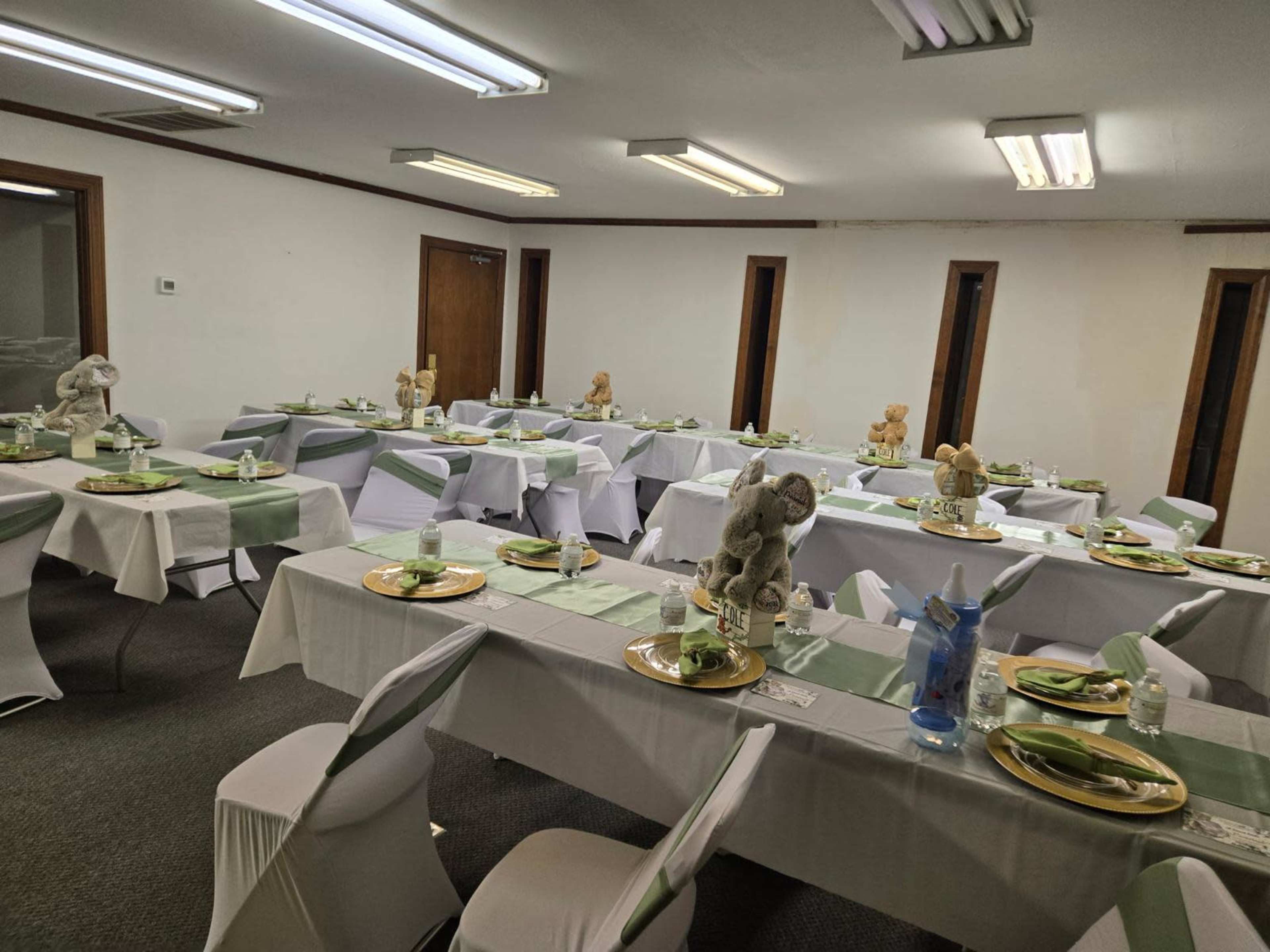 The image shows a dining room arranged with multiple tables, each set with plates, napkins, and small stuffed animals as centerpieces.