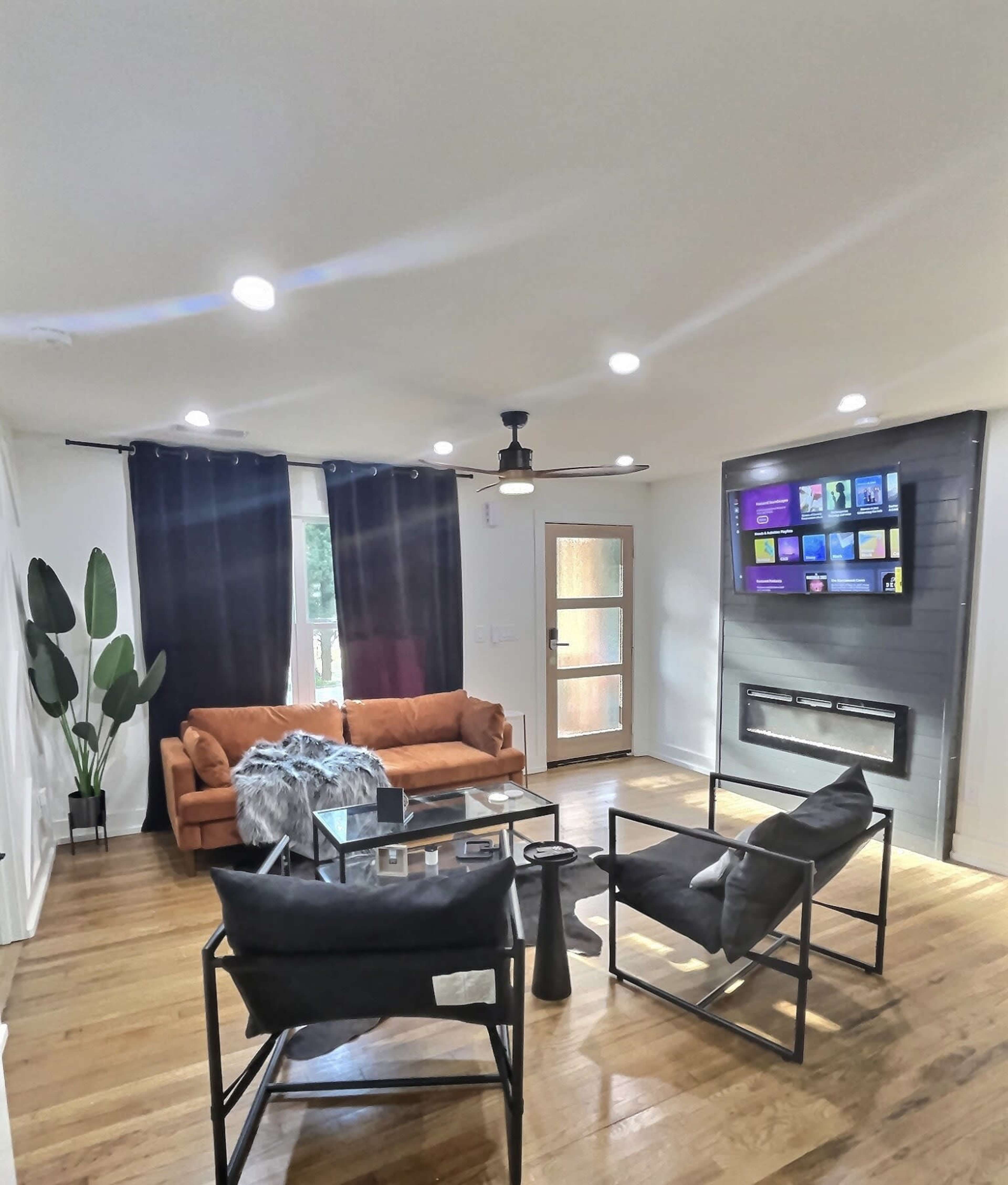 A modern living room with a brown couch, black chairs, a glass coffee table, and a mounted television above a fireplace.