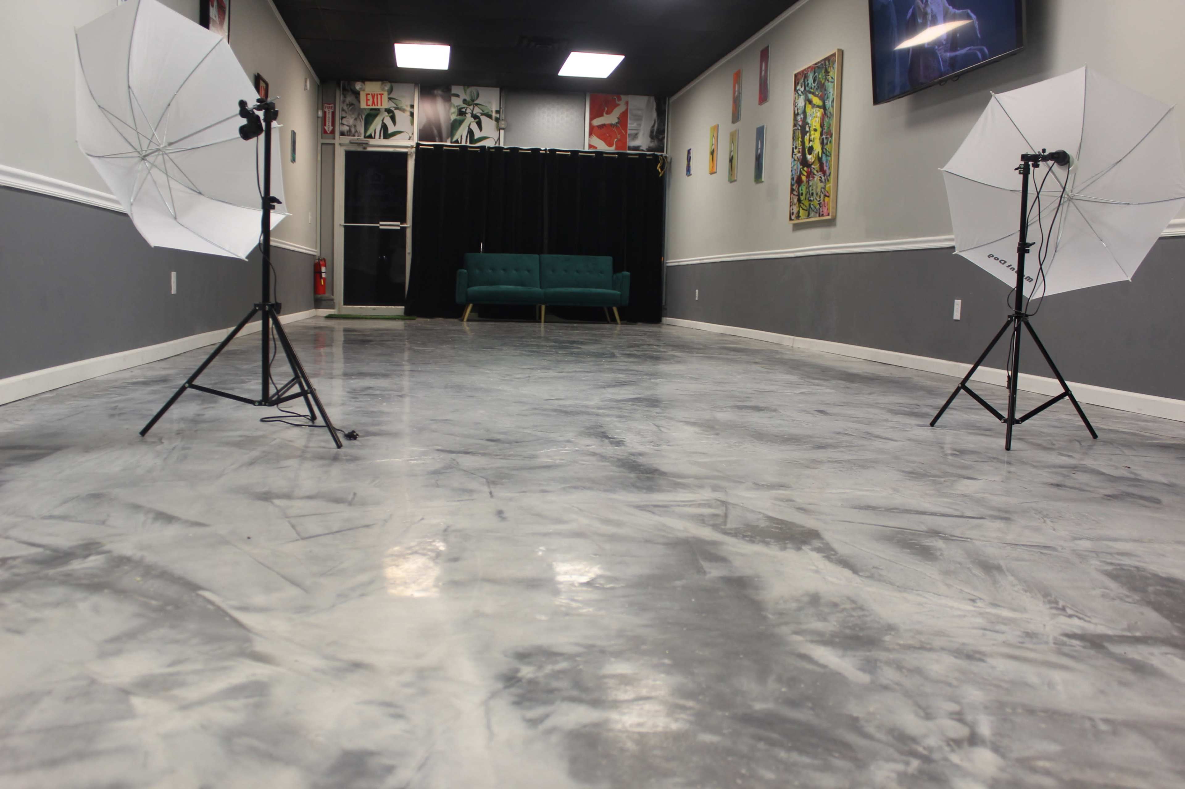 The image shows a spacious interior studio with a polished gray floor, a green sofa against a black curtain, and photography equipment placed on either side.