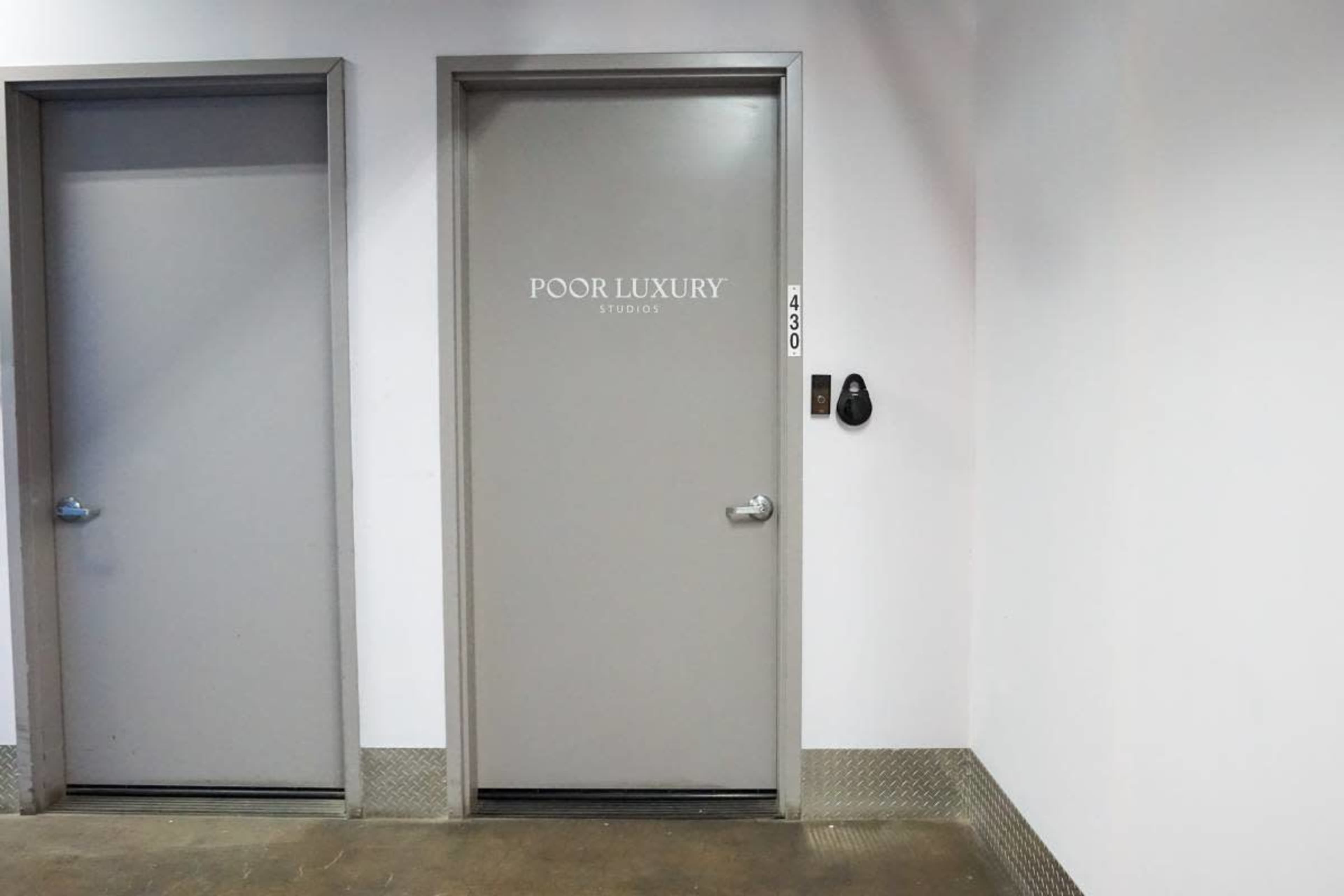 The image shows a gray door labeled "POOR LUXURY" next to another gray door in a hallway.