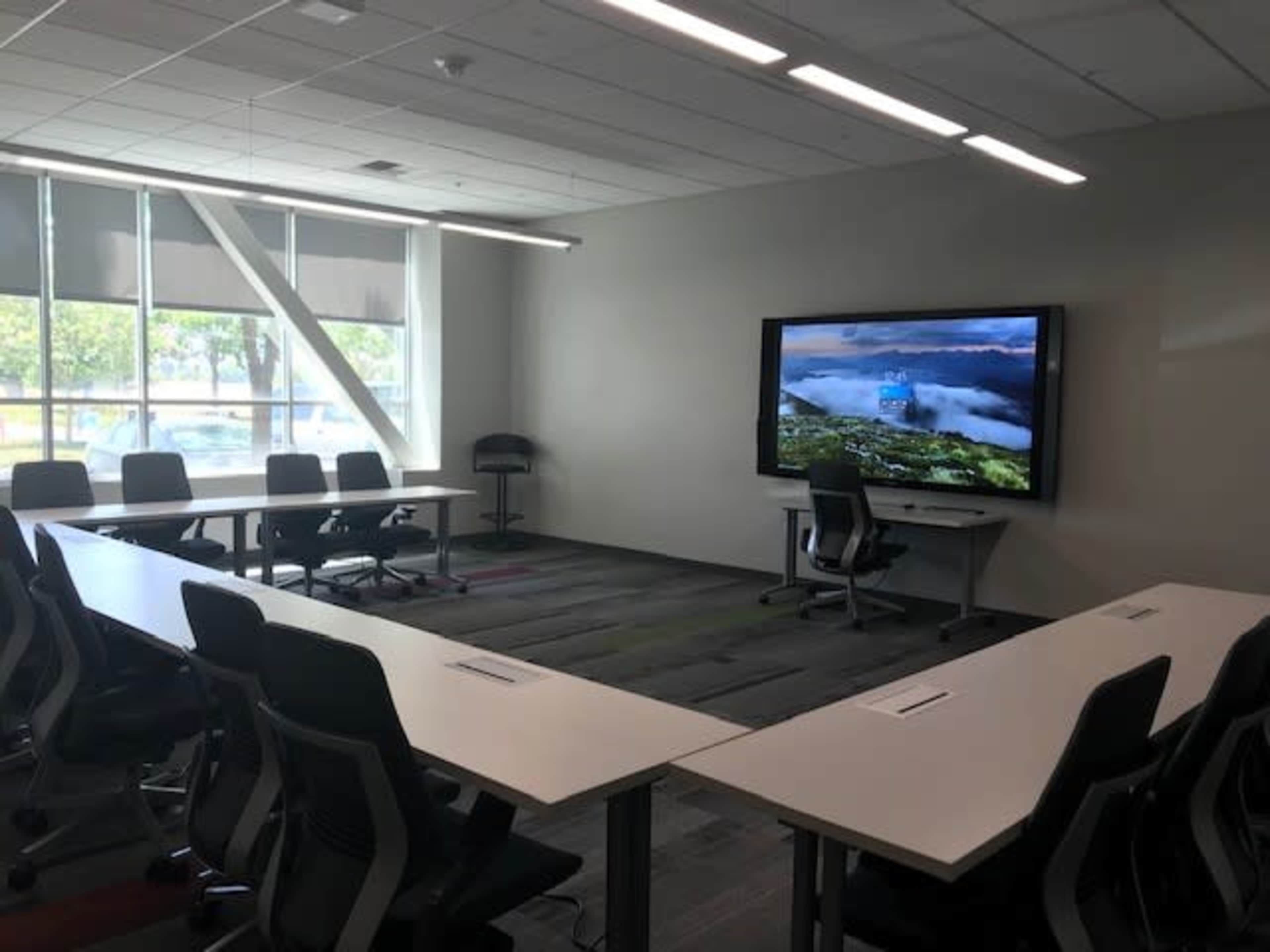 A modern conference room with several chairs and tables arranged in a U-shape around a large display screen.