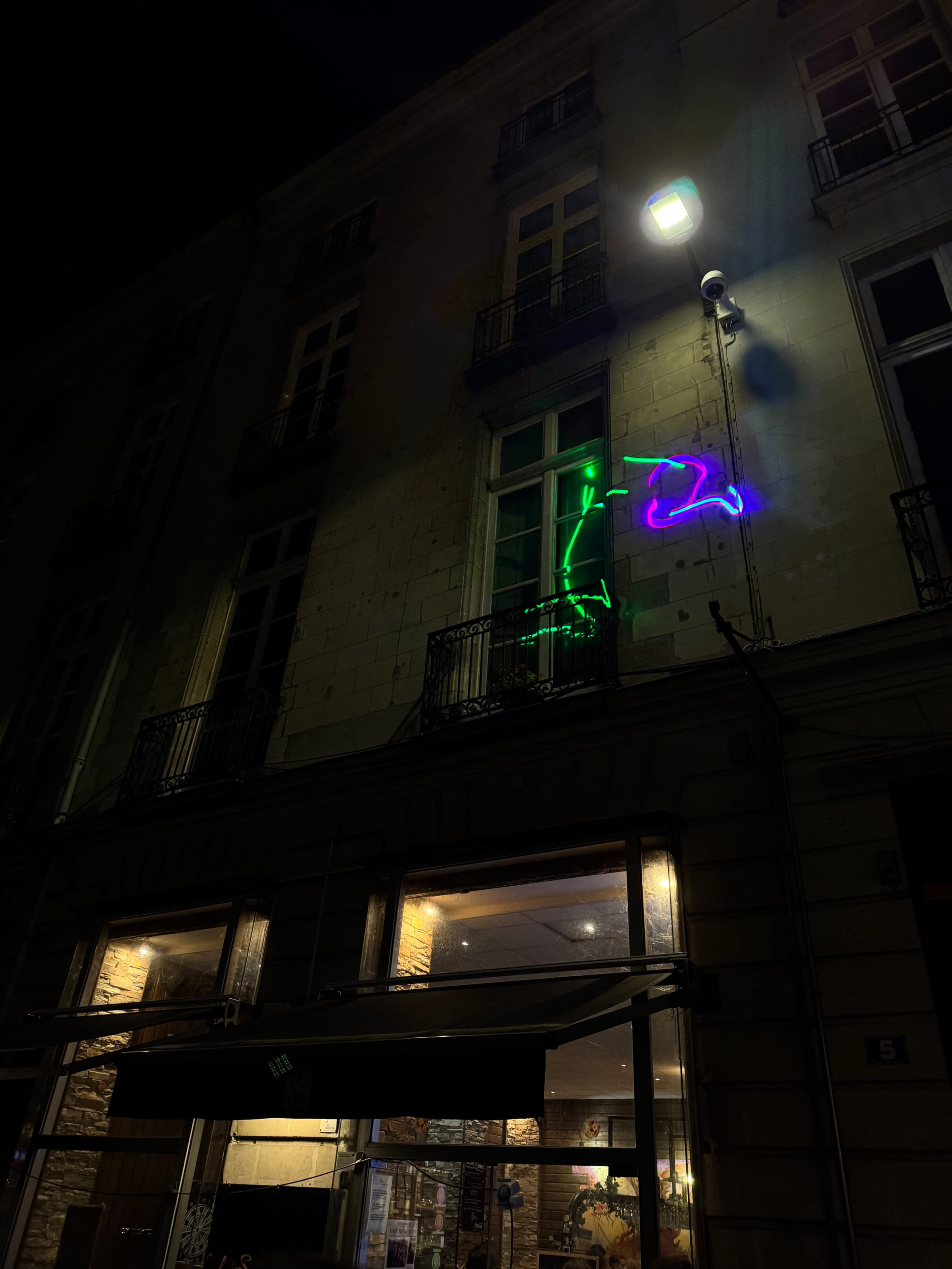 A neon green and purple light installation of a figure is displayed on the exterior wall of a building at night.