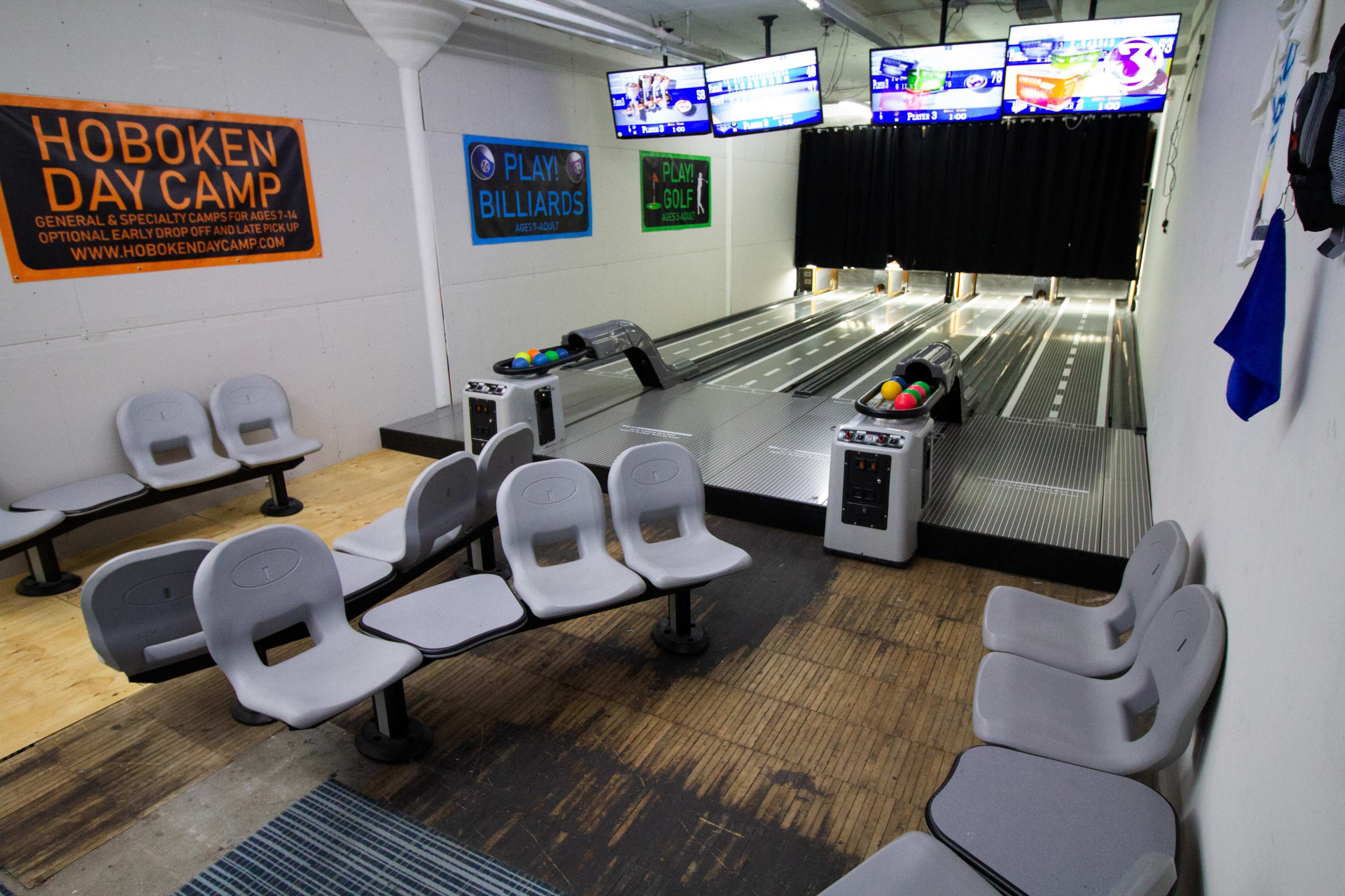 An indoor bowling alley with seating, wooden flooring, and multiple screens displaying scores.