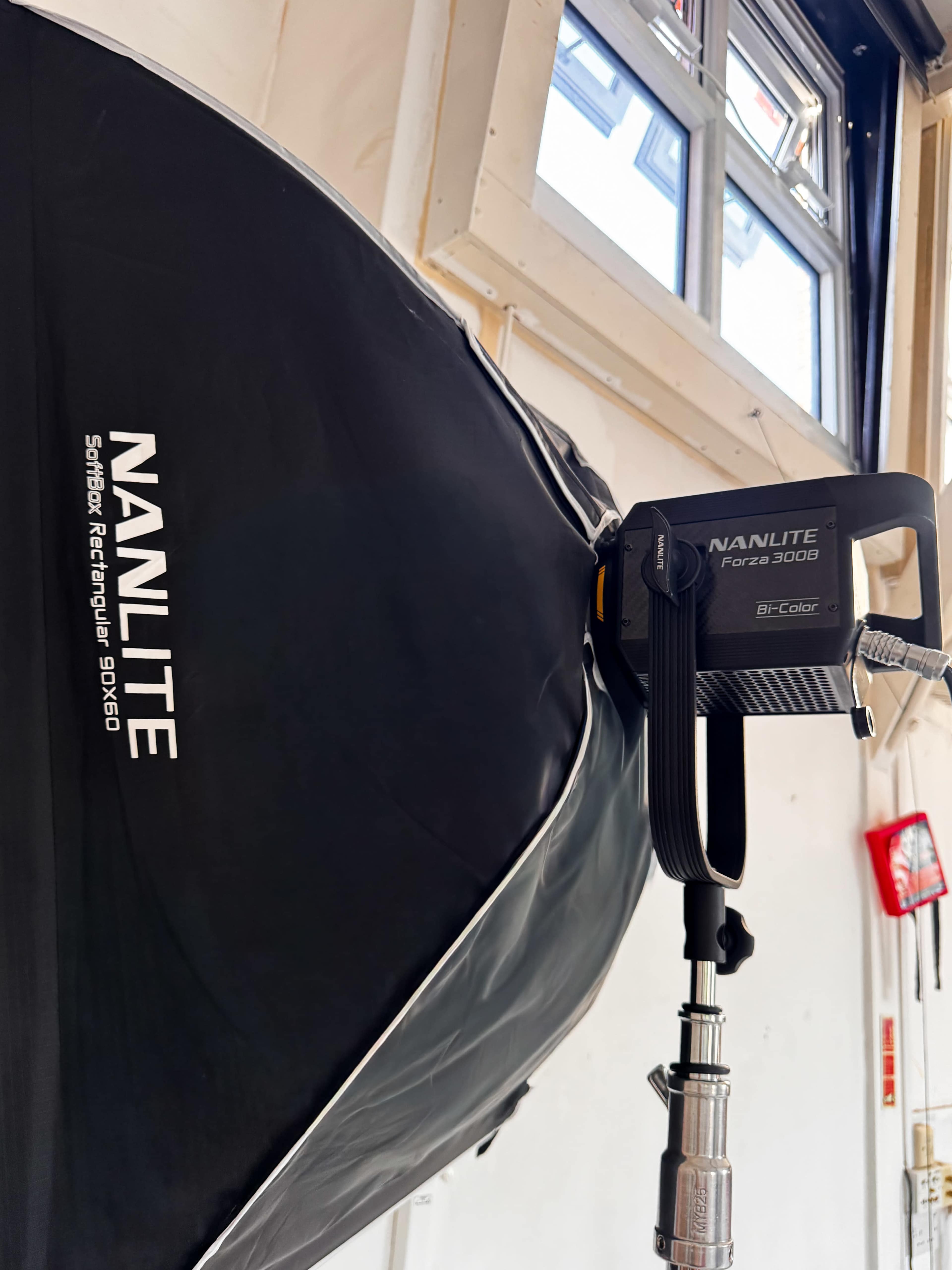 The image displays a NANLITE Force 300 LED light mounted on a softbox in a studio setting, with a window visible in the background.