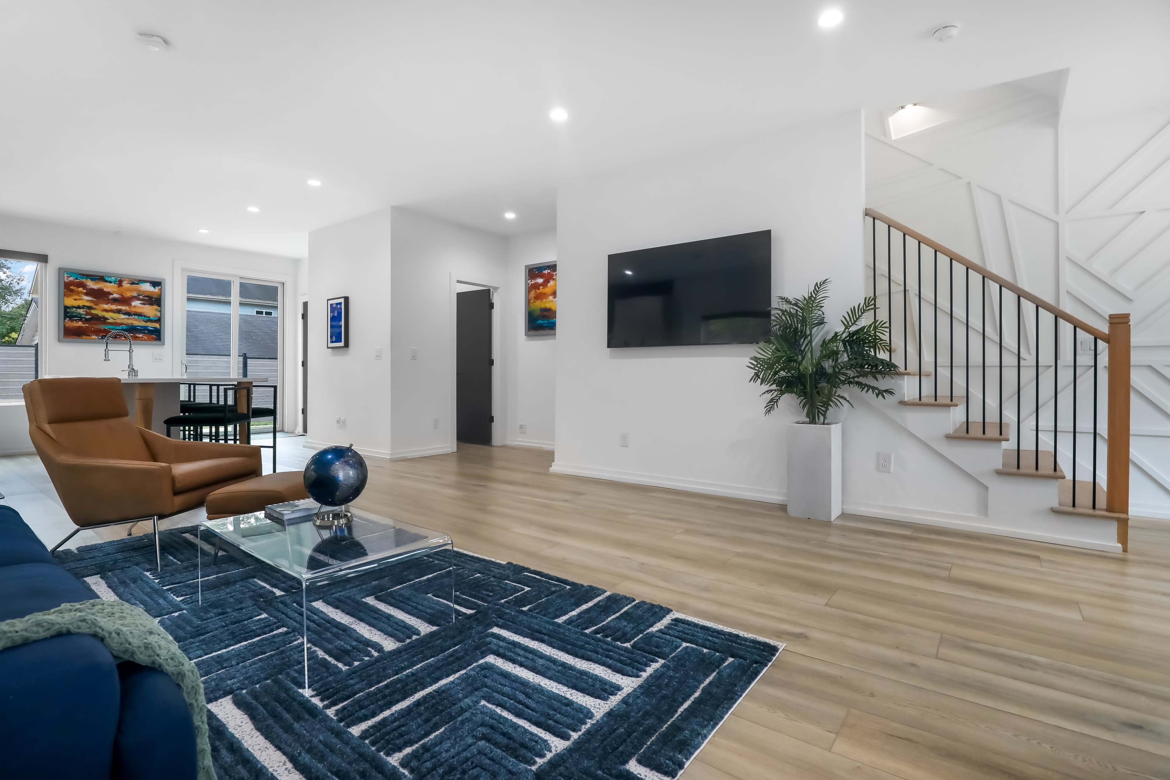 A modern living space featuring a blue area rug, a glass coffee table, a brown armchair, and a staircase leading to an upper level.