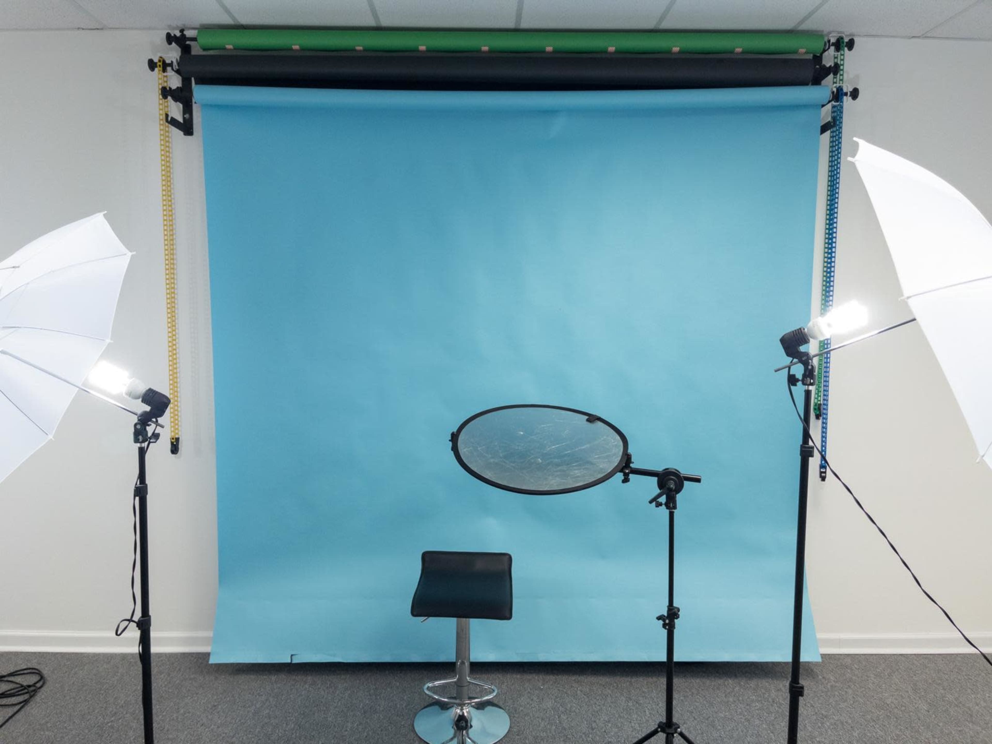 A photo studio setup with a blue backdrop, a black stool, and two light stands equipped with softboxes.