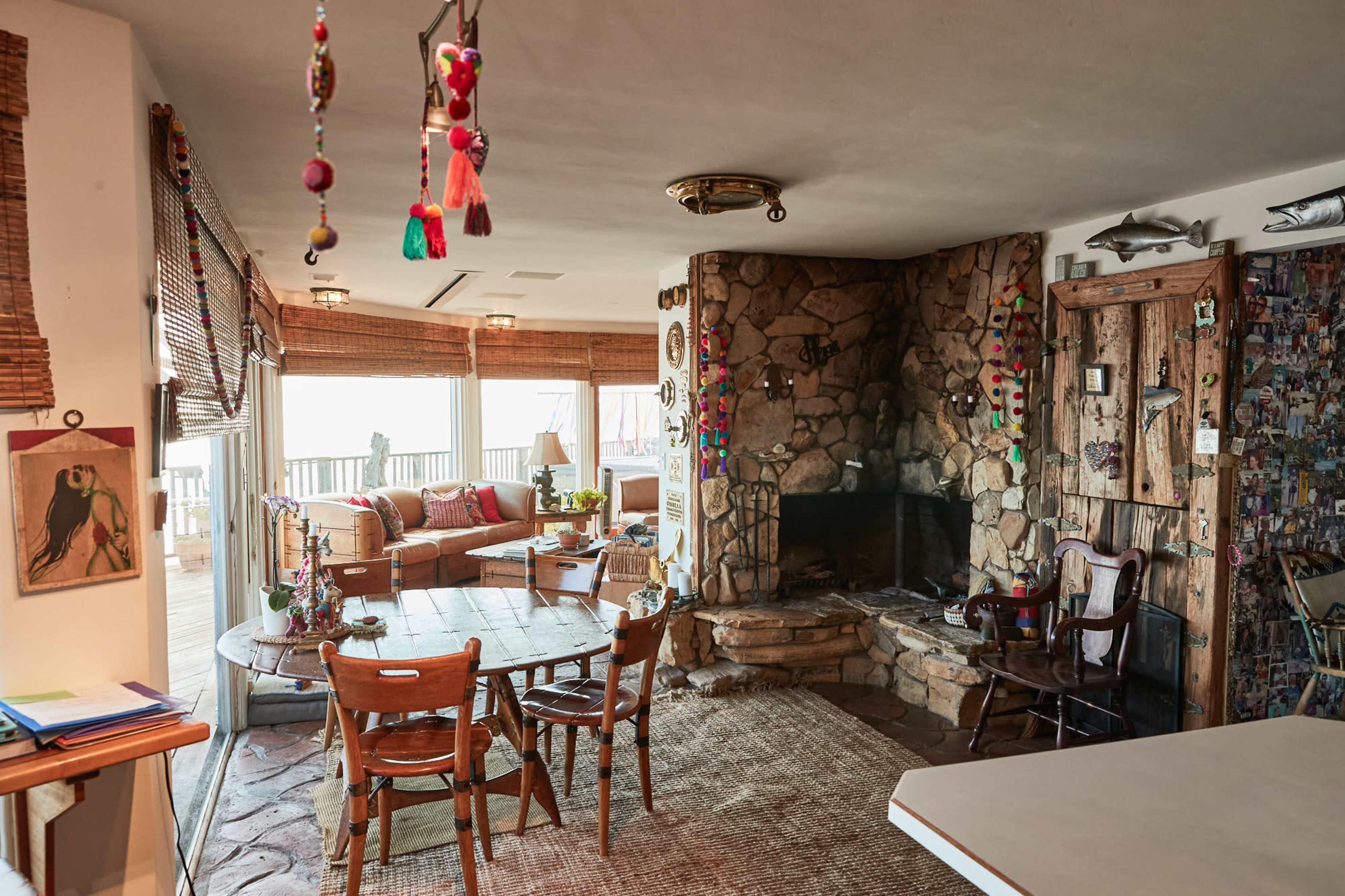 A cozy living space with a stone fireplace, wooden furniture, and a large window looking out onto a deck.