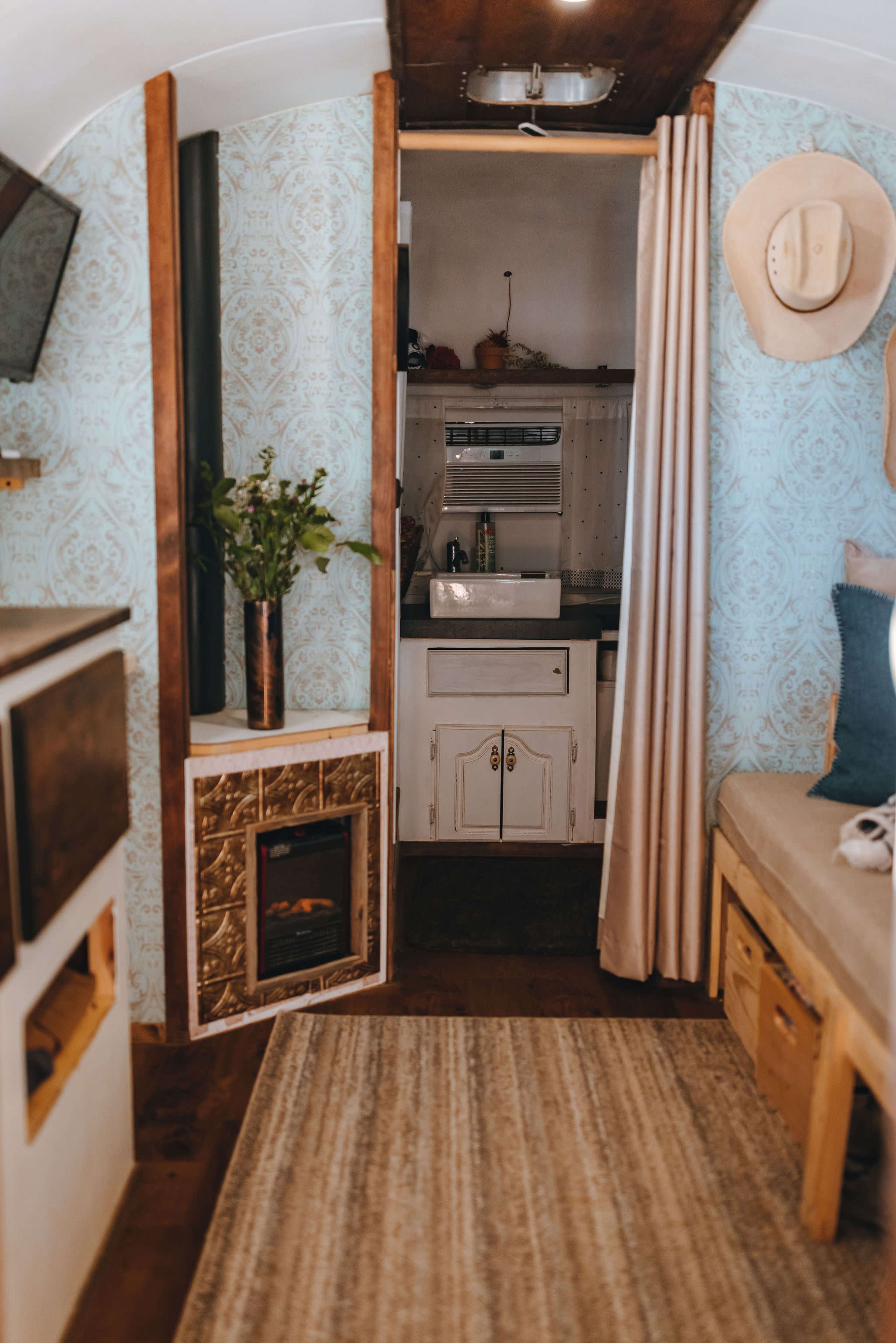 The interior of a vintage-style trailer features a cozy living area with a small kitchen and a decorative fireplace.