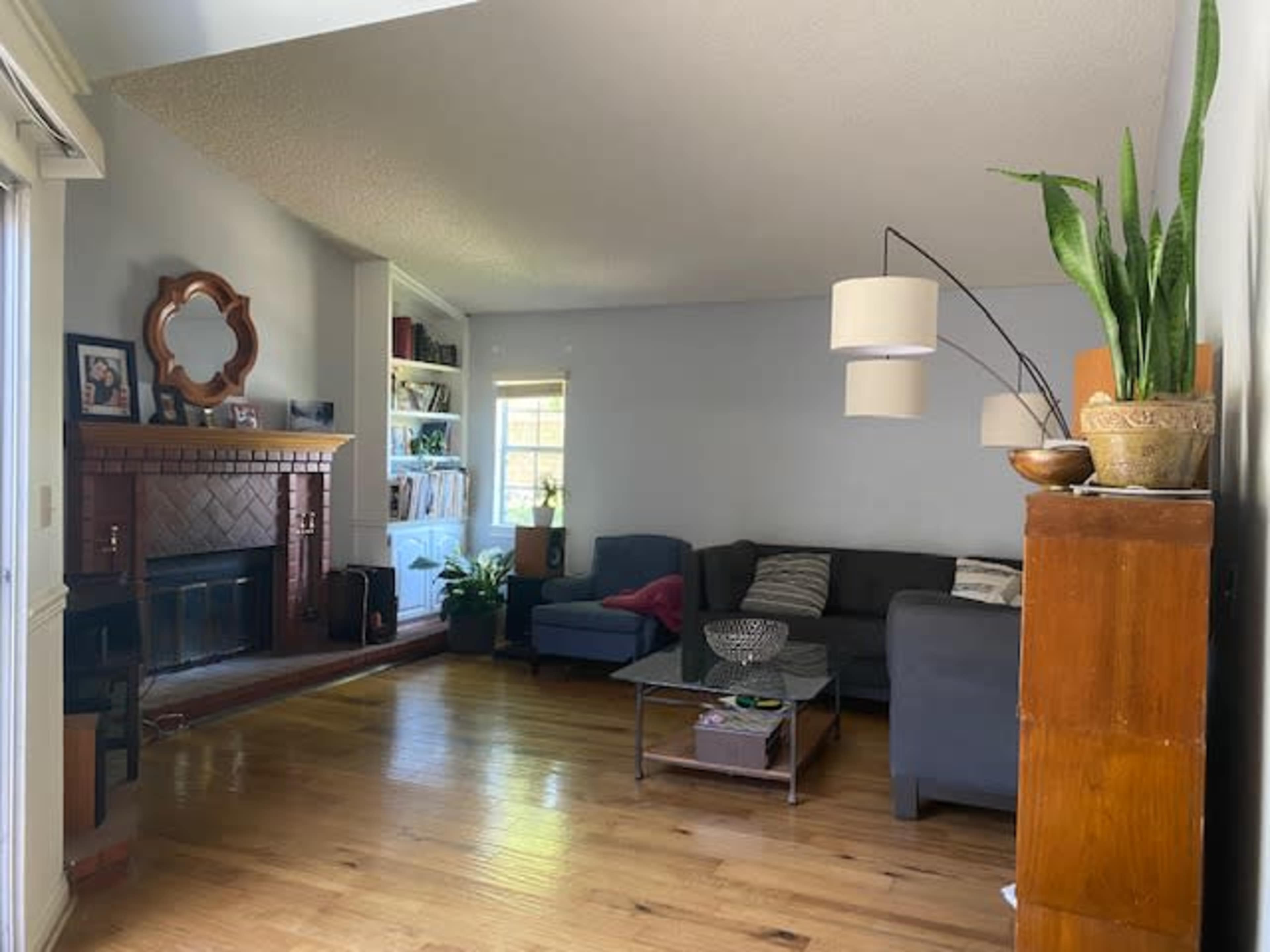 A living room features a sectional sofa, a coffee table, a fireplace, and shelves filled with books and decorative items.