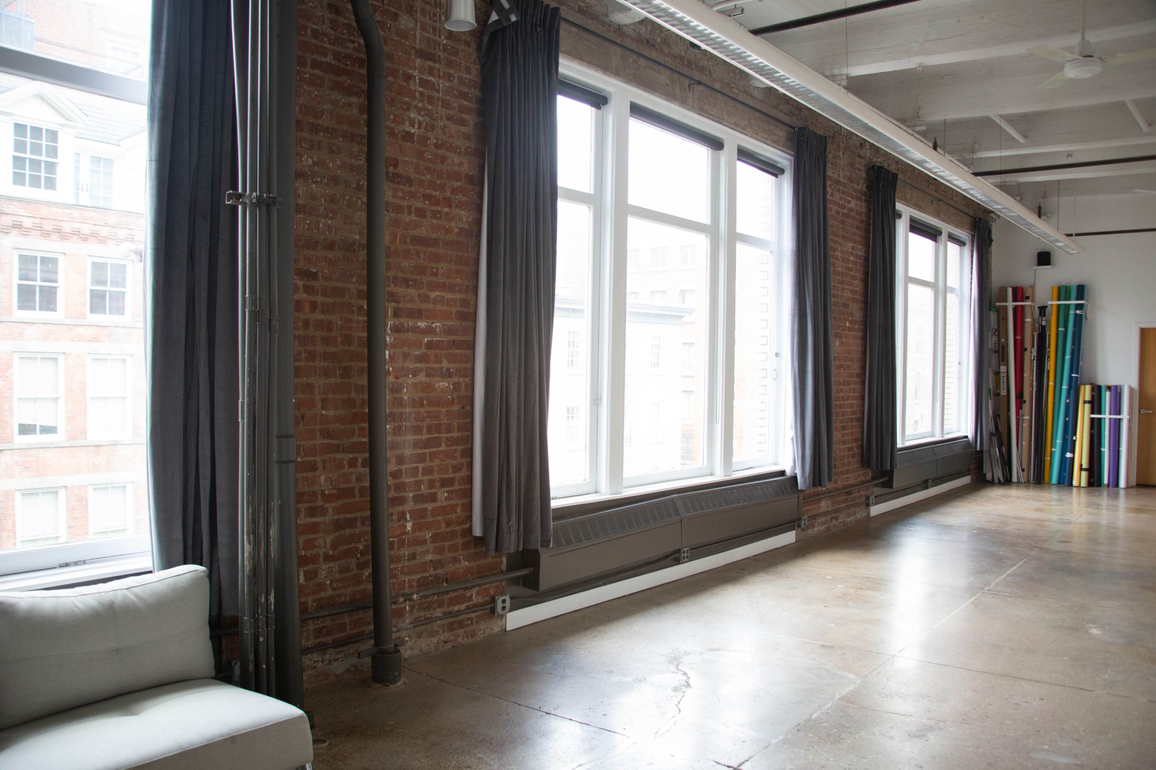A spacious room with large windows, exposed brick walls, and minimalist furniture.