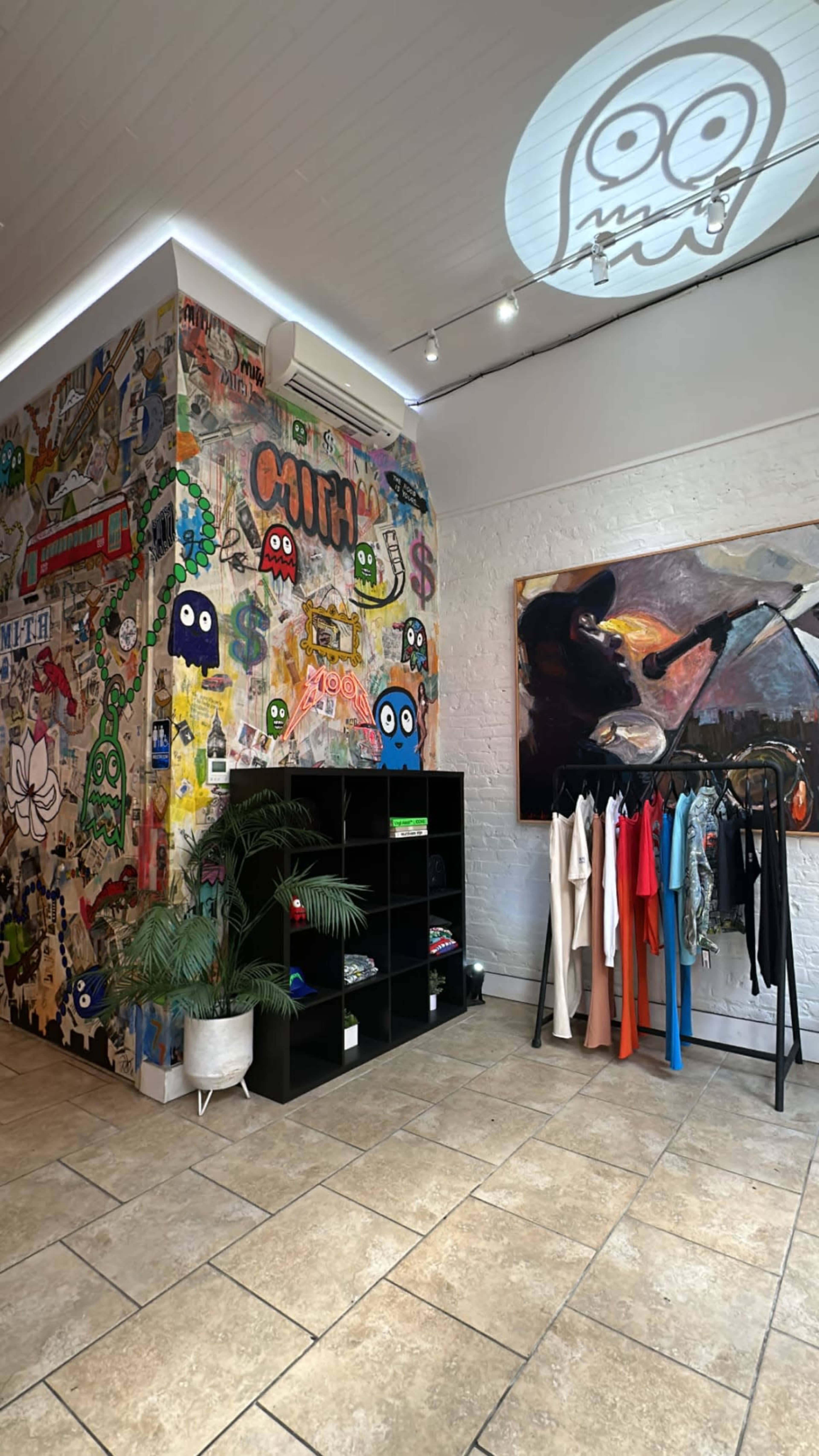 A retail space featuring a wall adorned with colorful graffiti and a section displaying clothing on racks next to a large artwork.