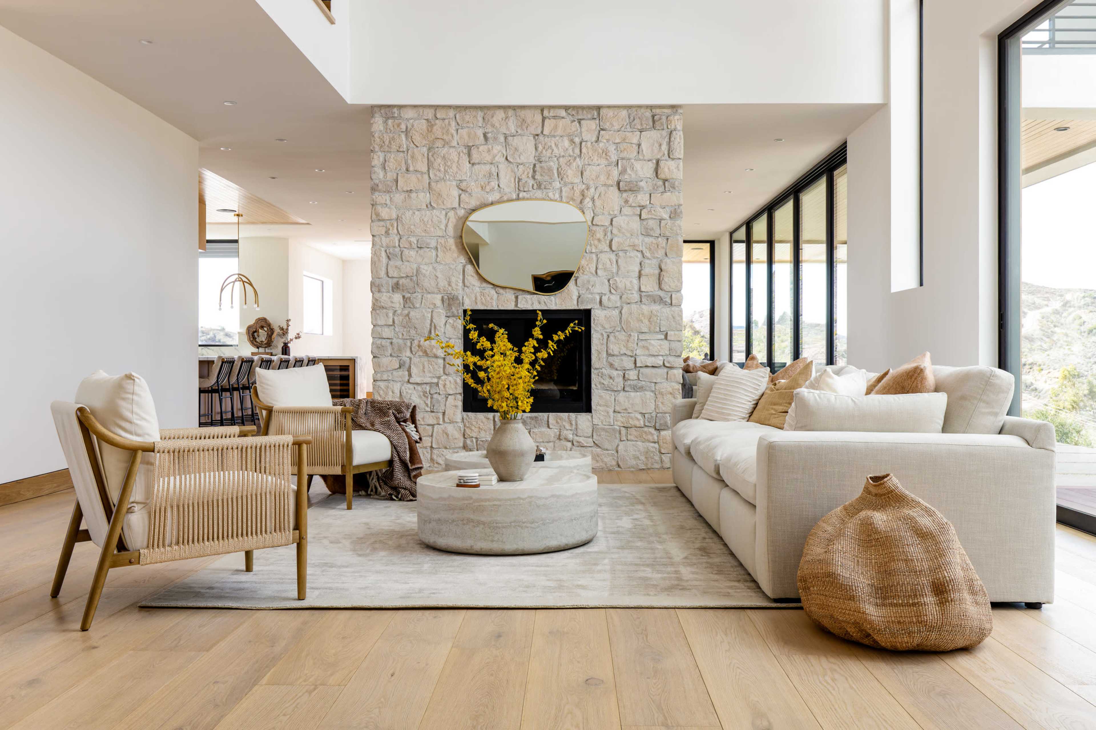 The image shows a modern living room with a stone fireplace, a beige sofa, and a round coffee table set on a light-colored rug.