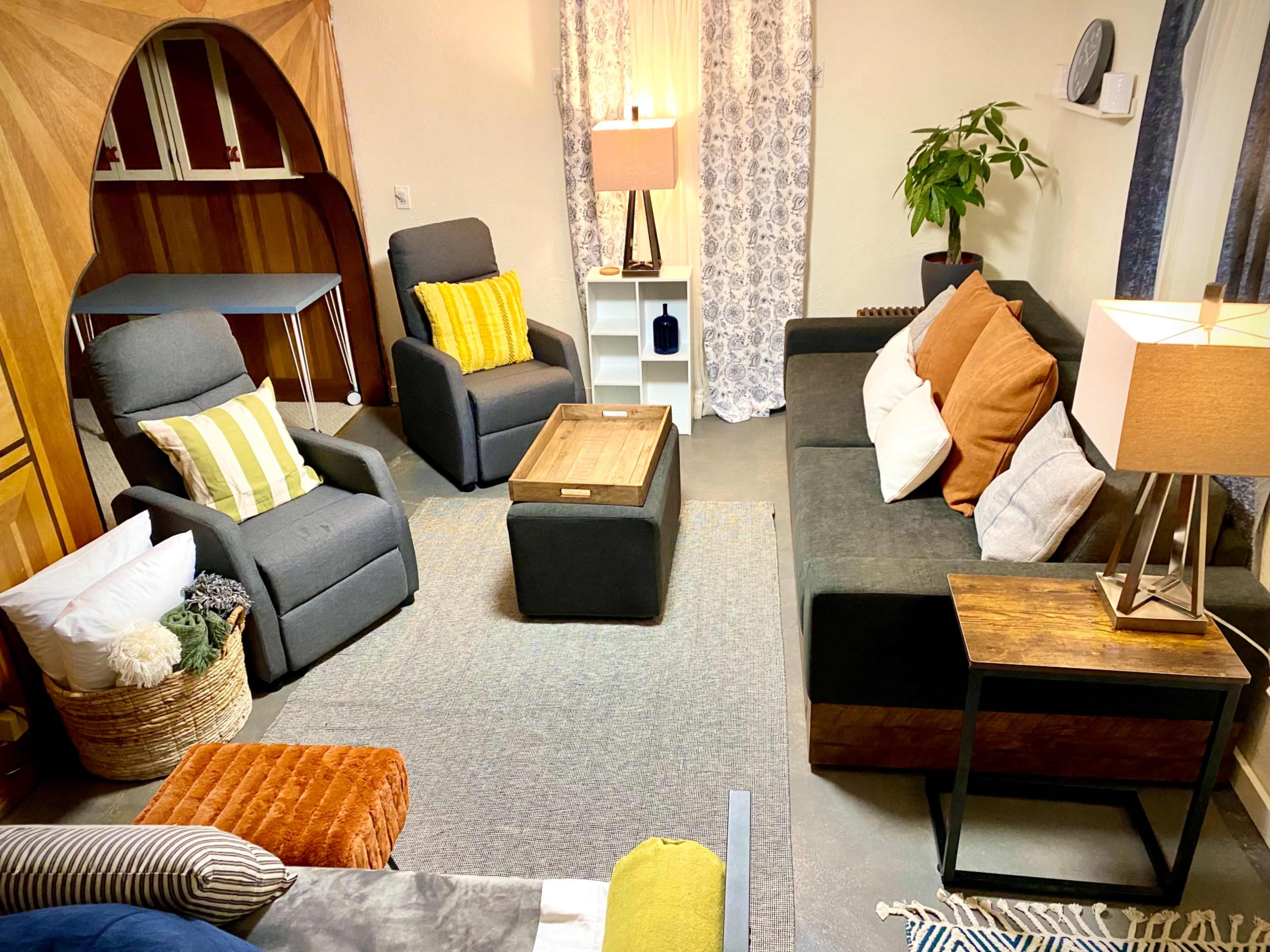A cozy living room setup with multiple seating options, a coffee table, and decorative elements, illuminated by soft lighting.