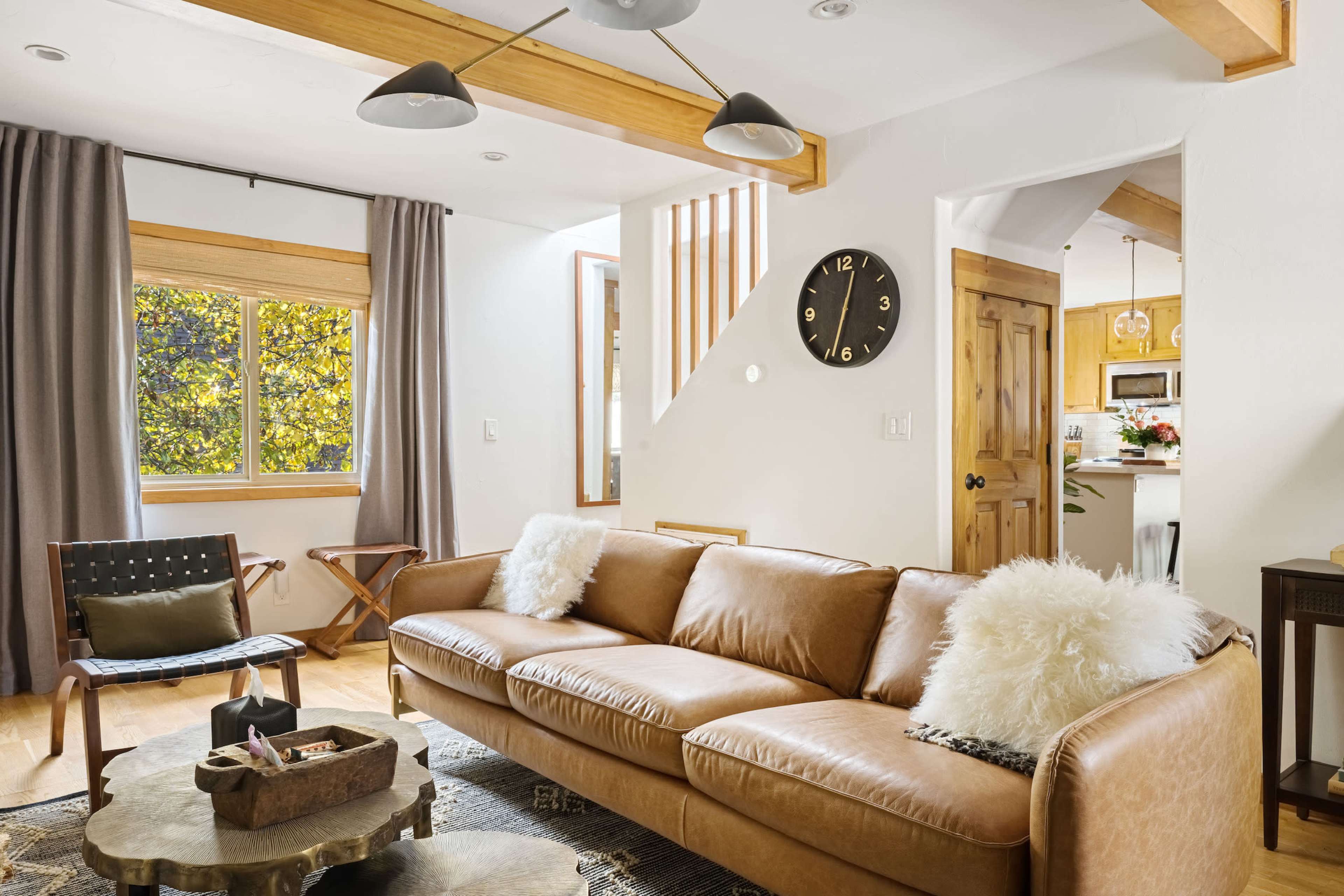 A modern living room with a brown leather sofa, a round coffee table, and a large window revealing an outdoor view.
