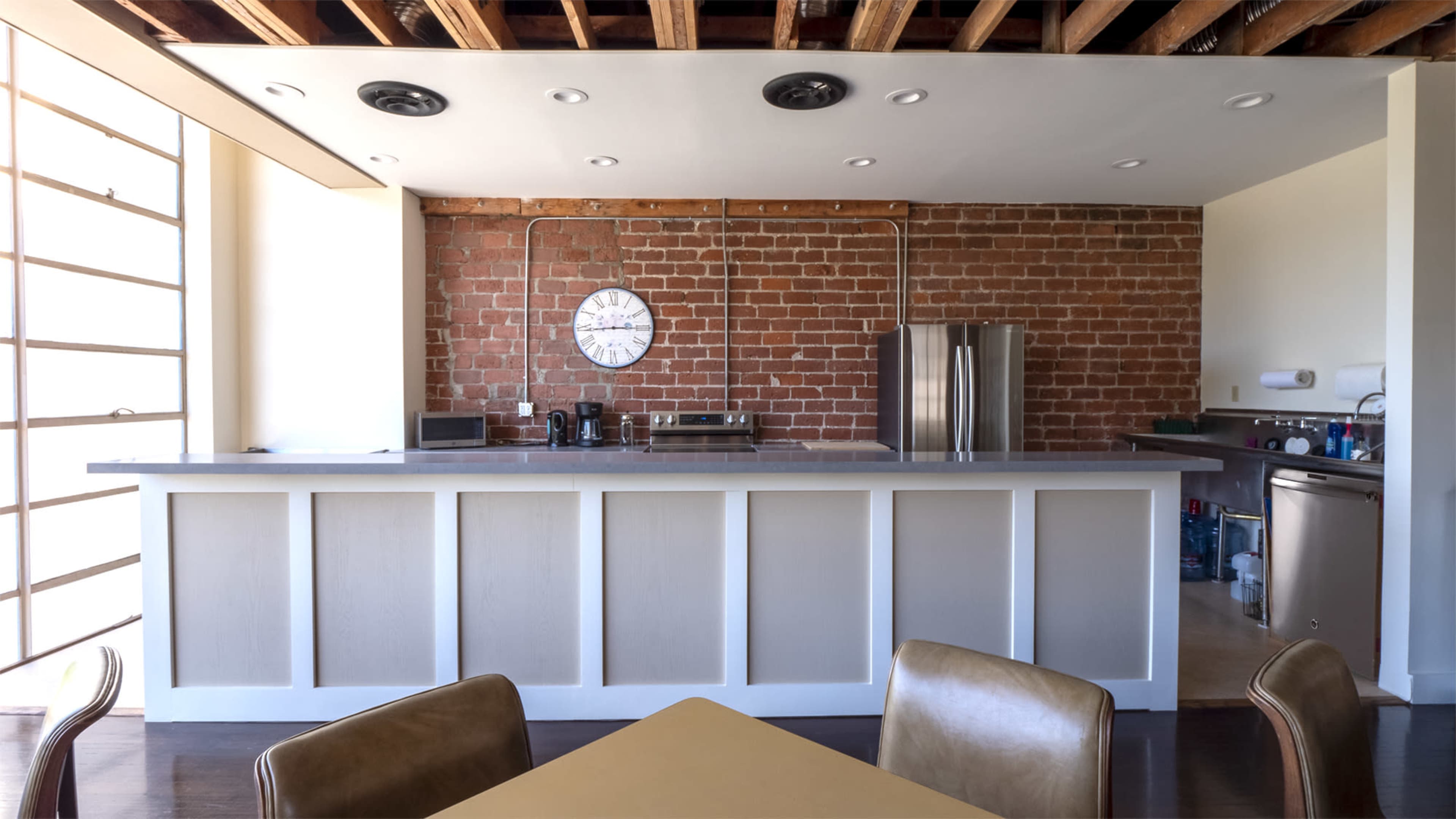A modern kitchen with a brick wall, a sleek countertop, stainless steel appliances, and a round wall clock.