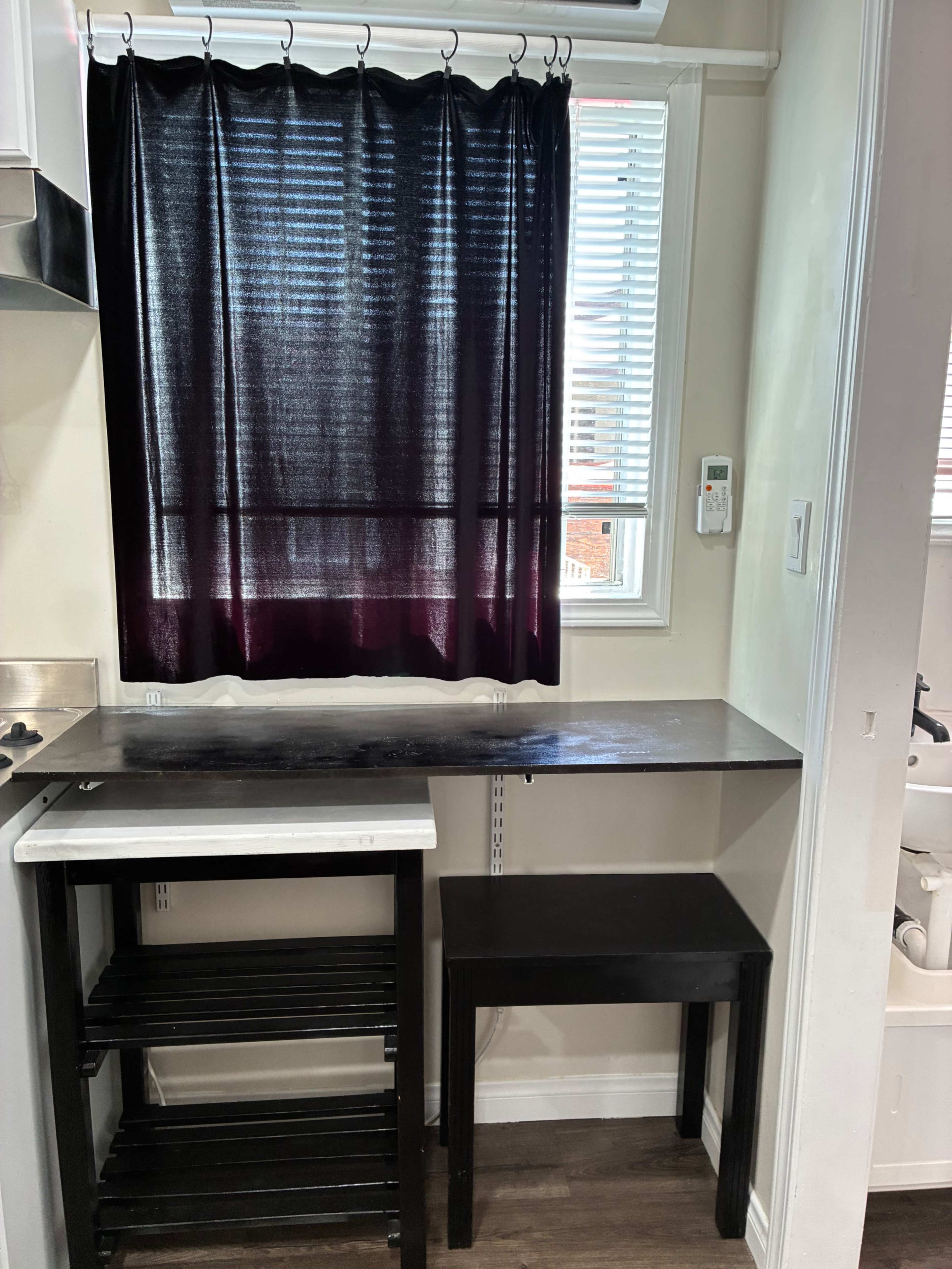 The image shows a small kitchen area with a countertop, a black table, and a curtain covering a window.