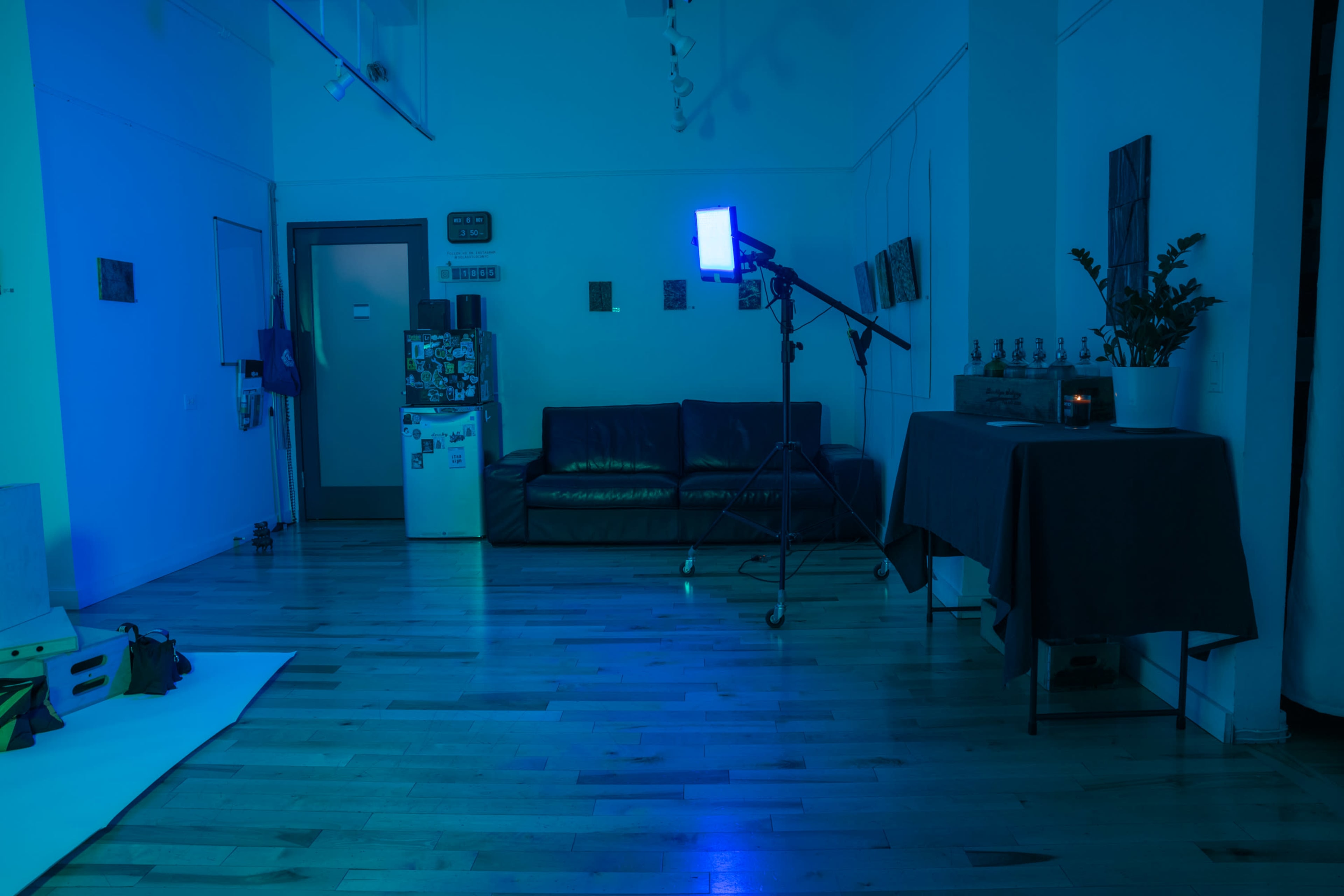The image shows a dimly lit room with blue lighting, featuring a sofa, a standing light, a table, and a refrigerator.