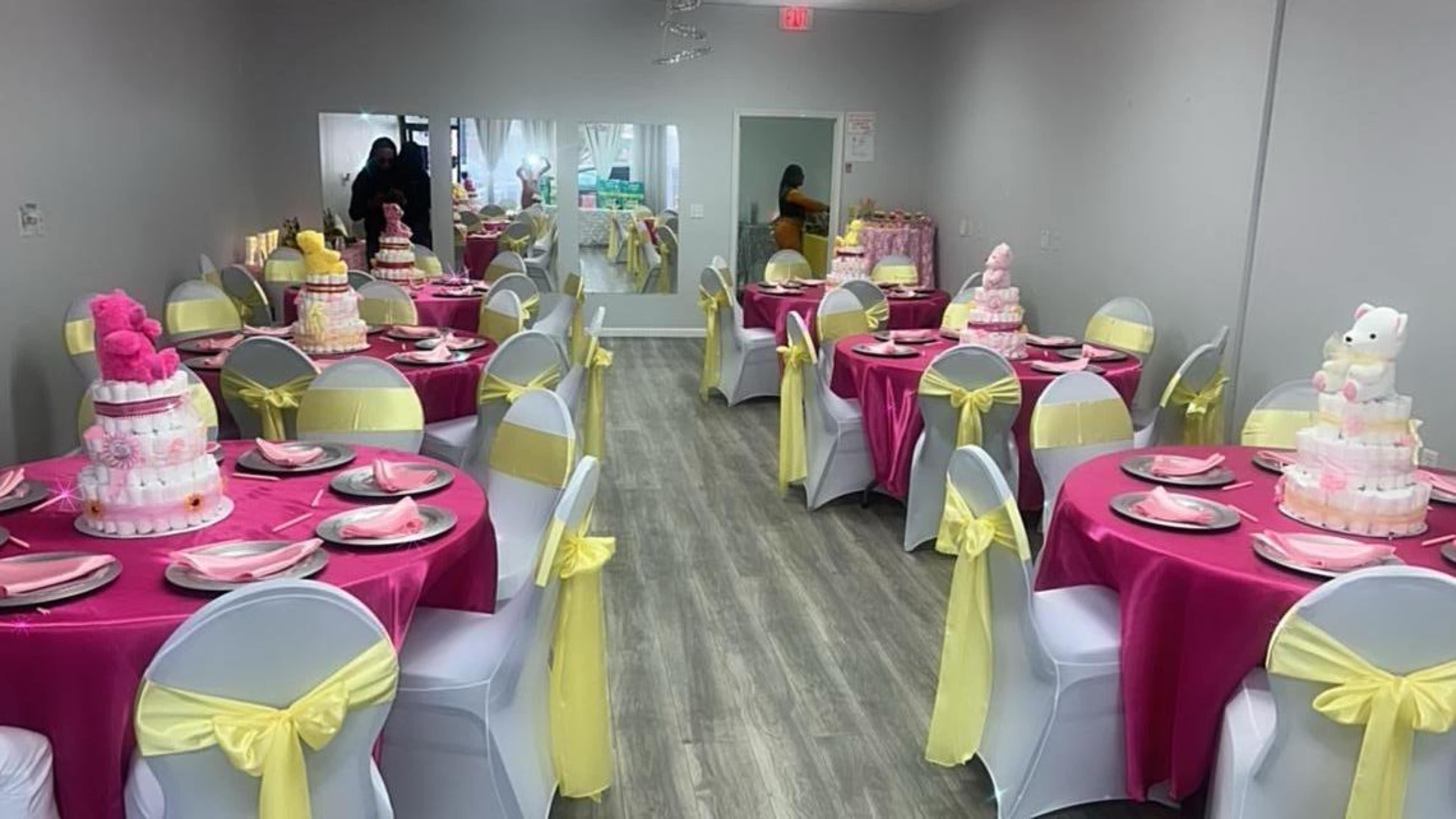A decorated party room with pink and yellow tablecloths, each set with plates, and featuring multiple multi-tiered cakes on display.