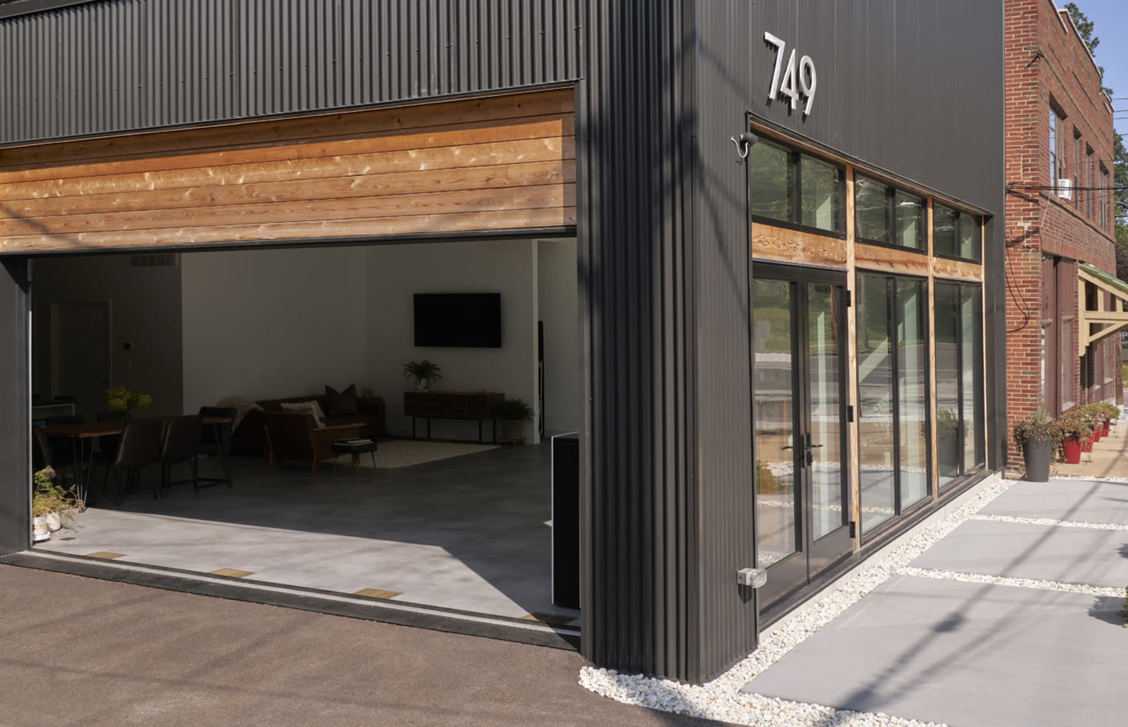 The image features a modern building with large glass doors partially open, revealing an interior space and a landscaped exterior with stone pathways.