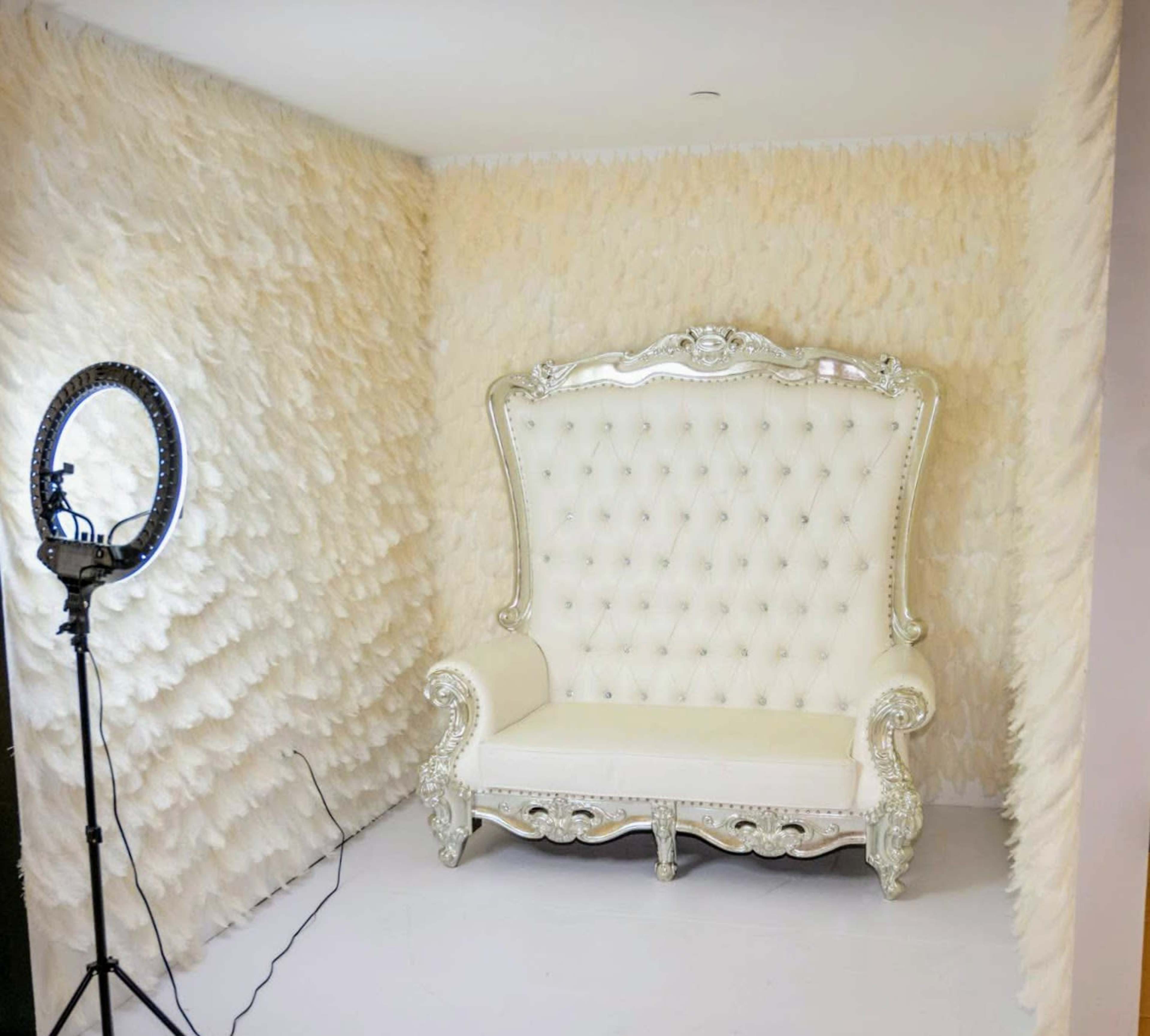 A luxurious white tufted sofa with ornate silver detailing, positioned in a room with textured, pale beige walls.