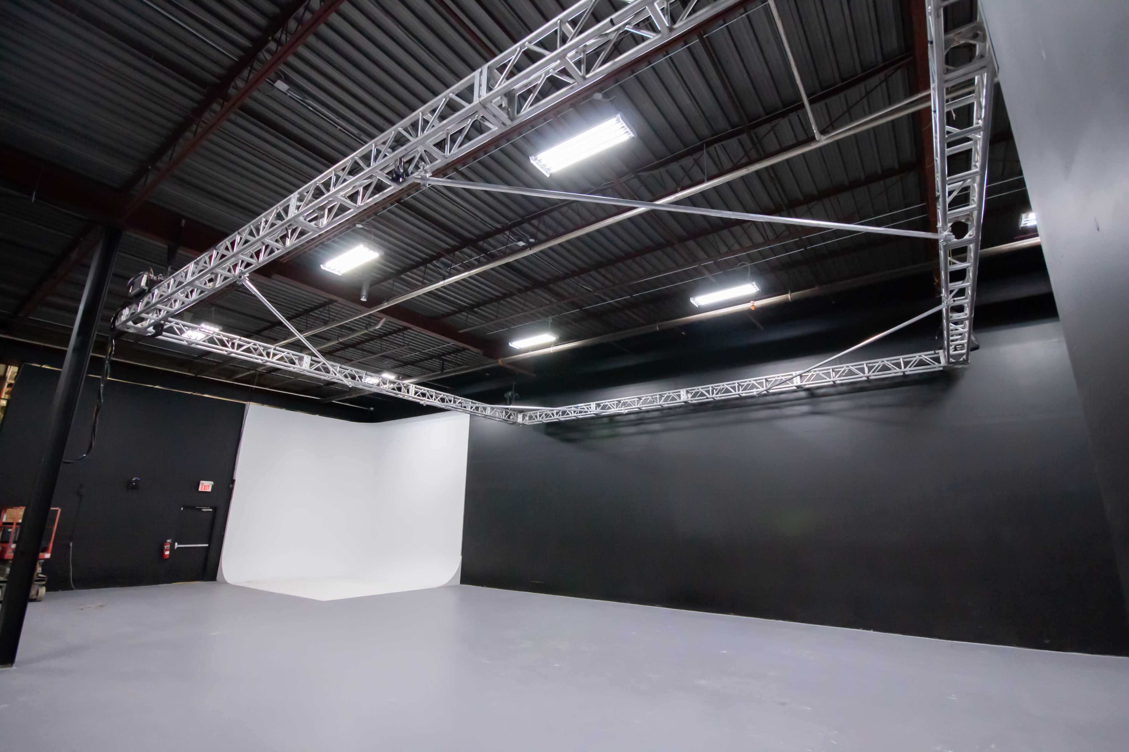 An empty studio space with a white backdrop and a grid of overhead lighting rigged from the ceiling.