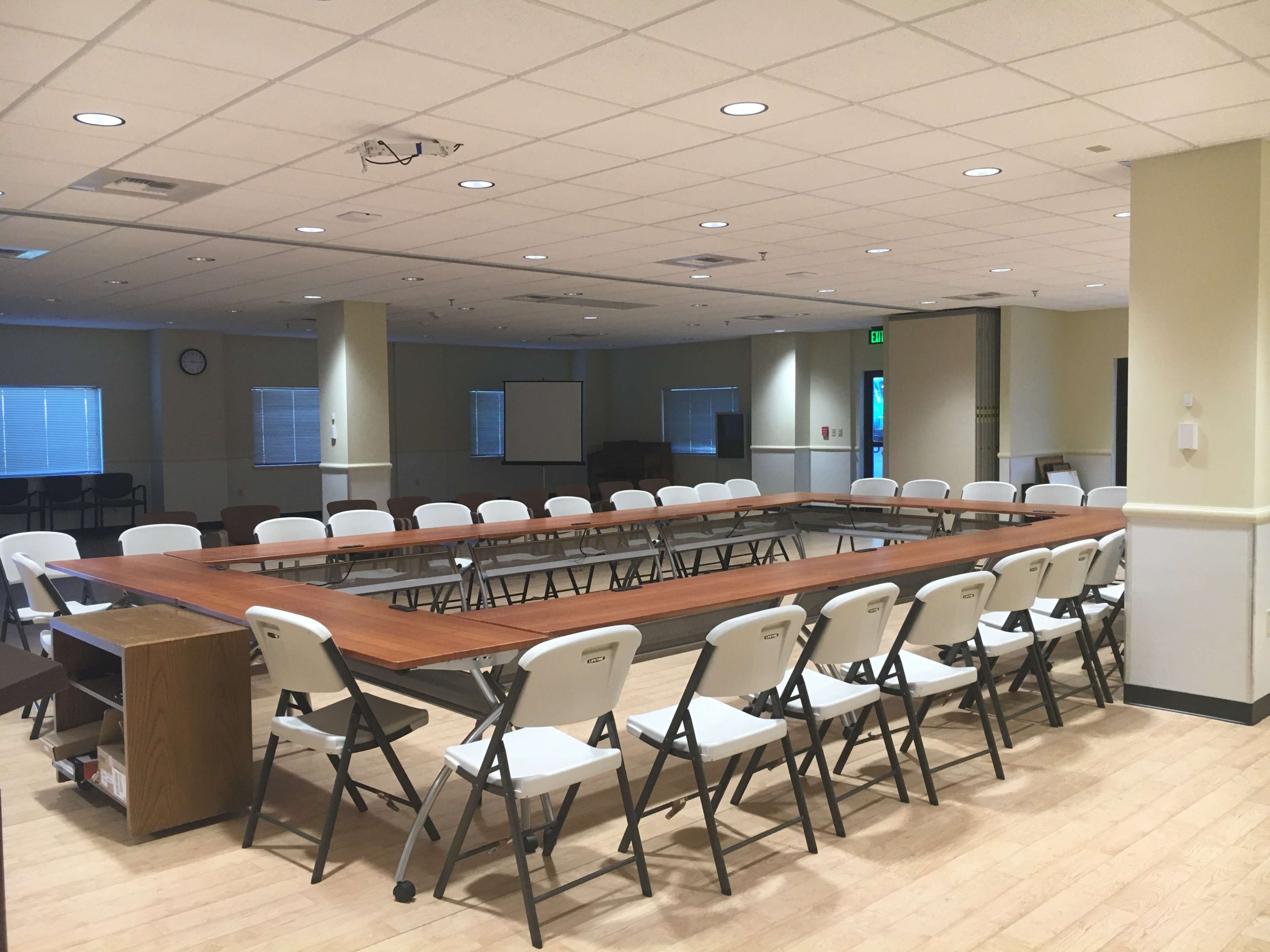A meeting room with a large rectangular table surrounded by folding chairs and large windows.