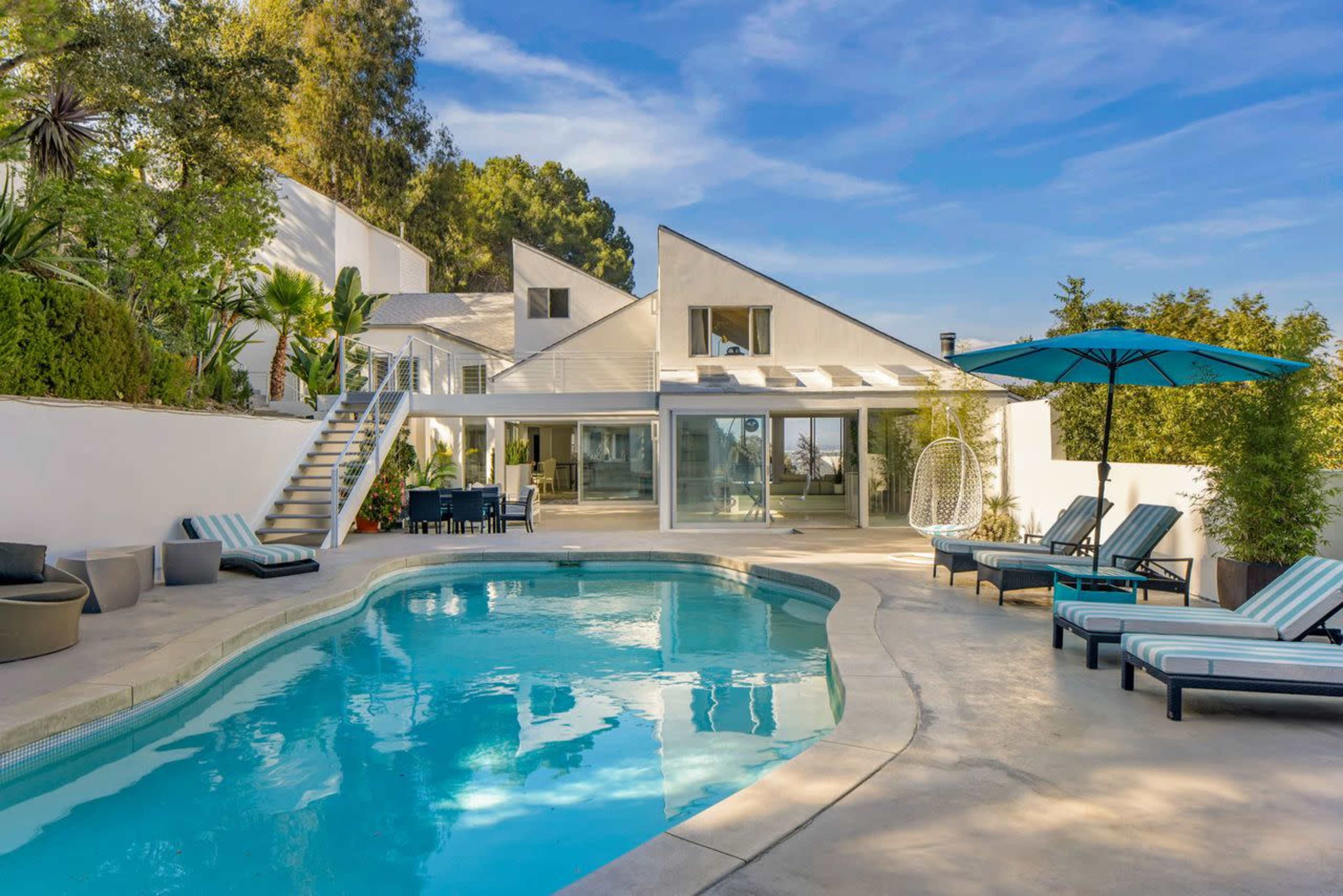 A modern house with a pool, outdoor seating area, and landscaped greenery is set against a clear blue sky.