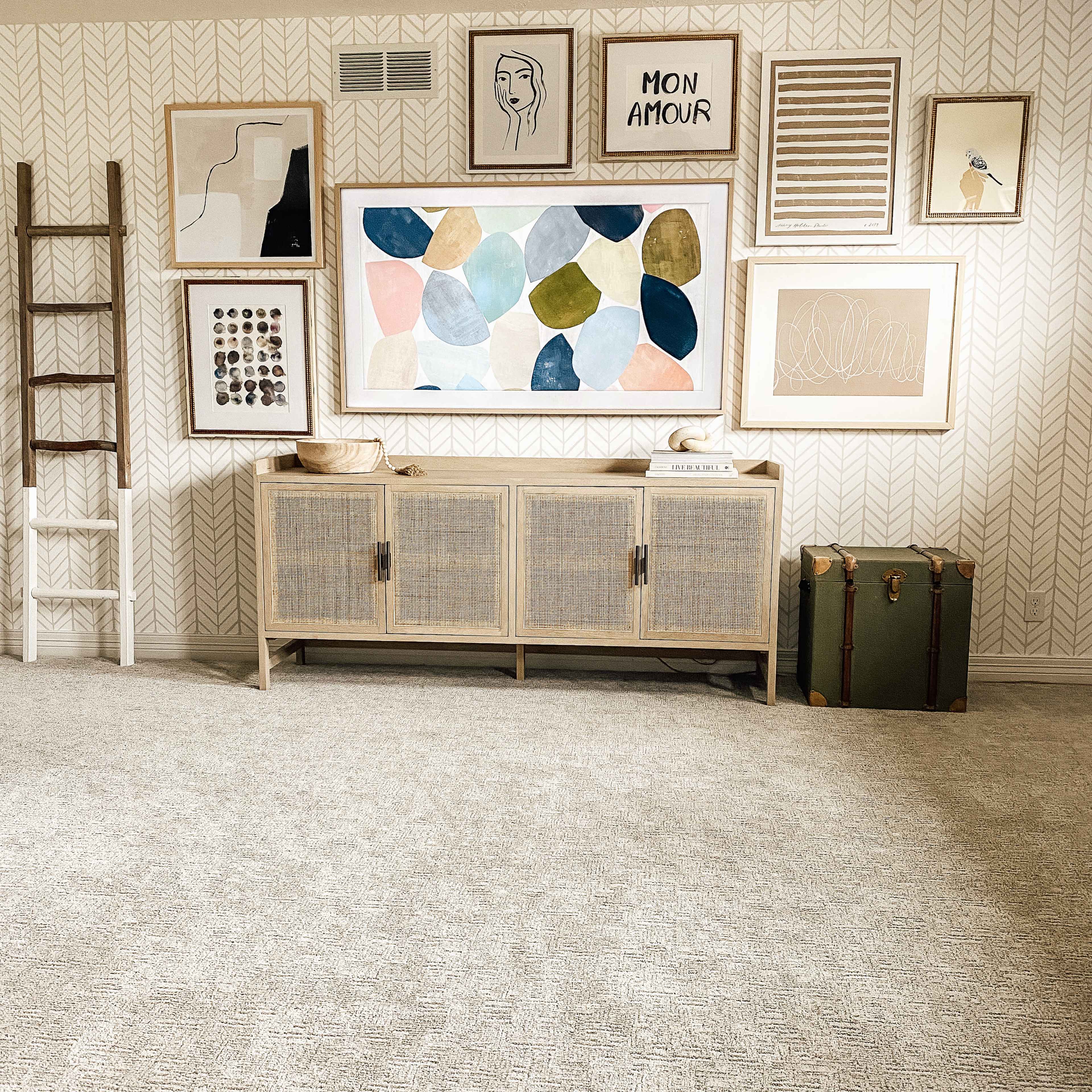 The image shows a neatly decorated living room featuring a low cabinet, a collection of framed artworks, and a decorative ladder against a textured wall.
