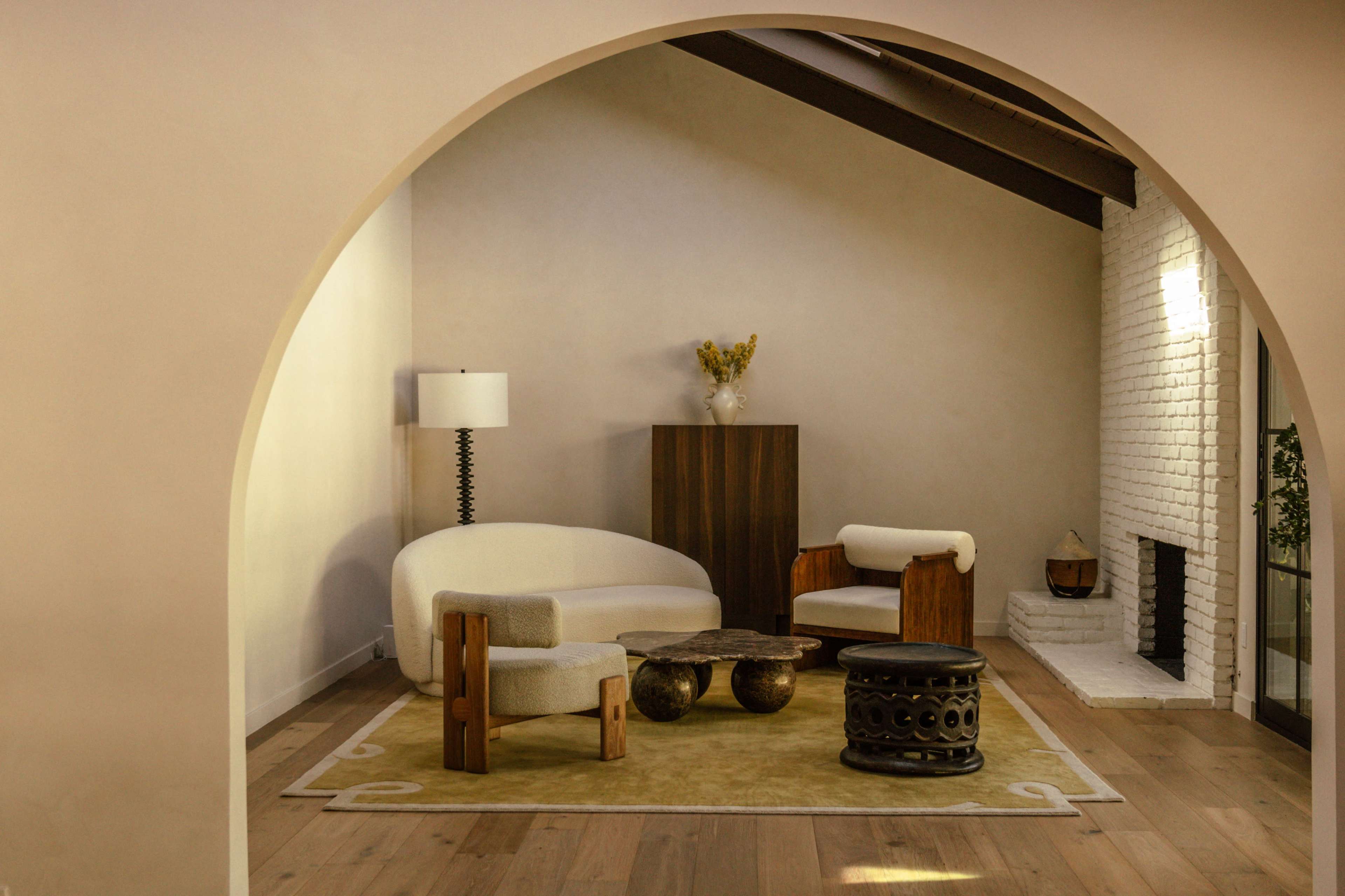 The image shows a minimalist living room with a curved archway, featuring a white sofa, a wooden cabinet, and a round coffee table on a yellow area rug.