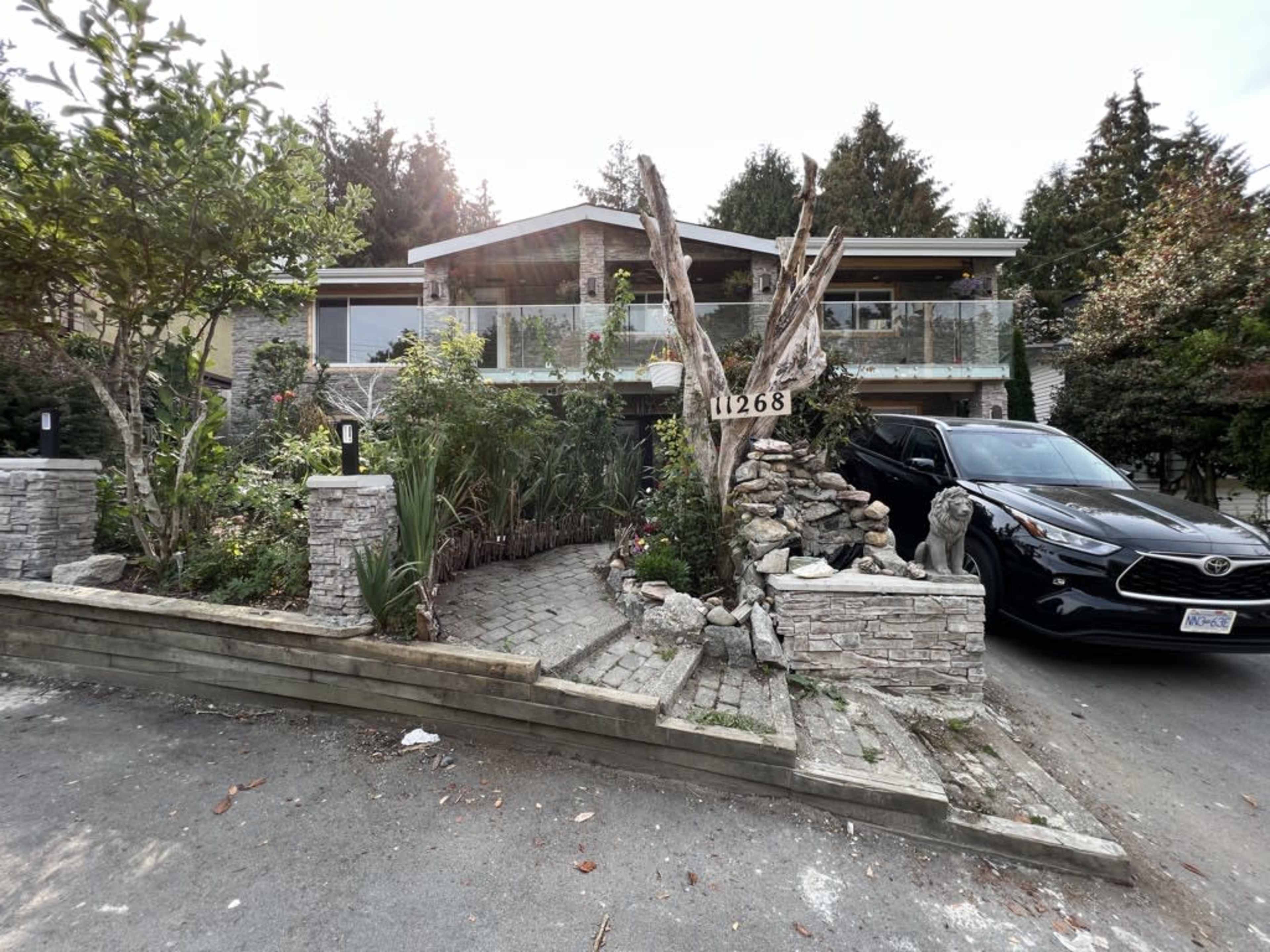 A modern house with a stone pathway, landscaped gardens, and a black car parked in the driveway.