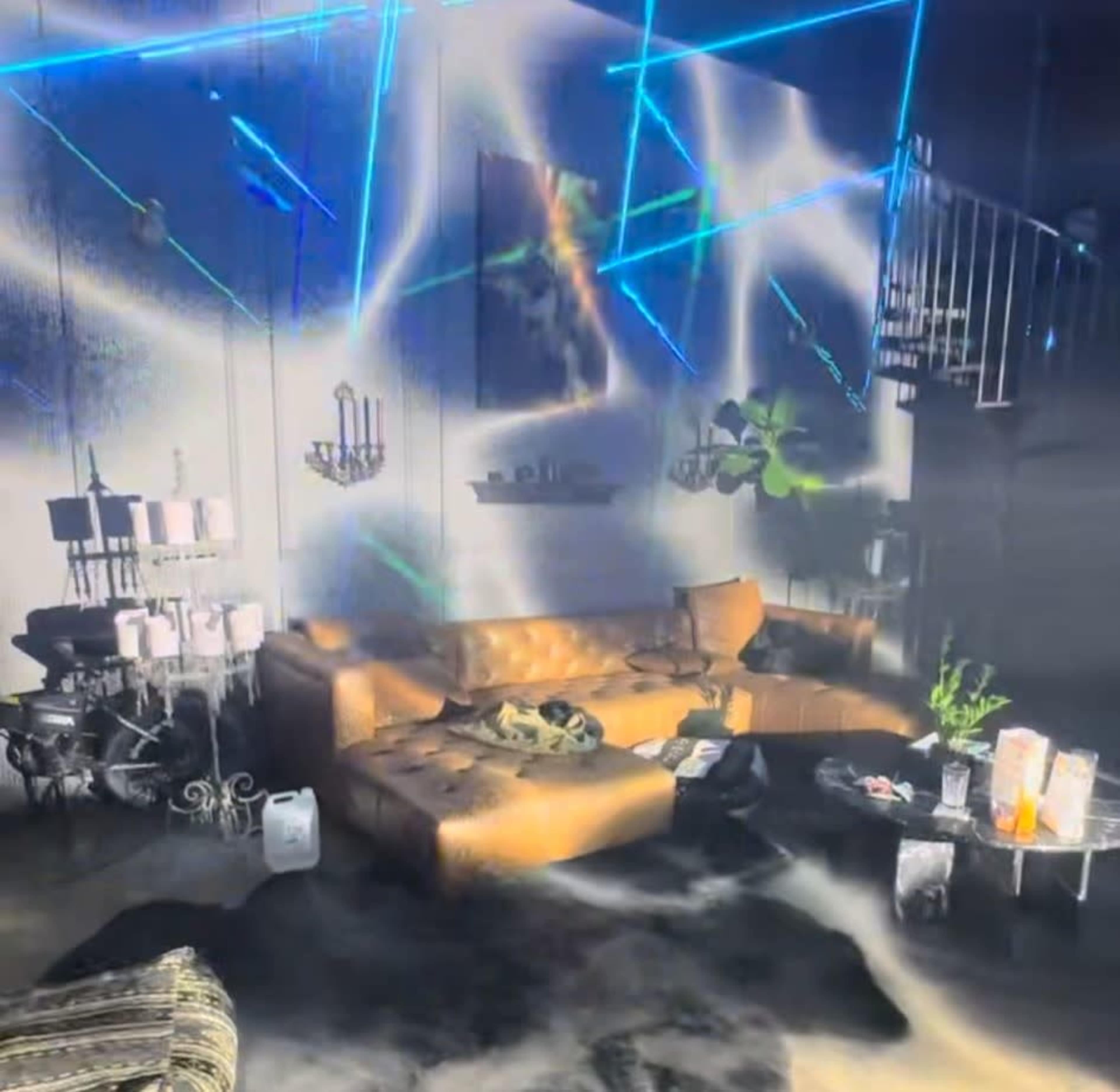 A foggy living room features a brown leather couch, a glass coffee table with candles, and blue laser lights projecting on the walls.