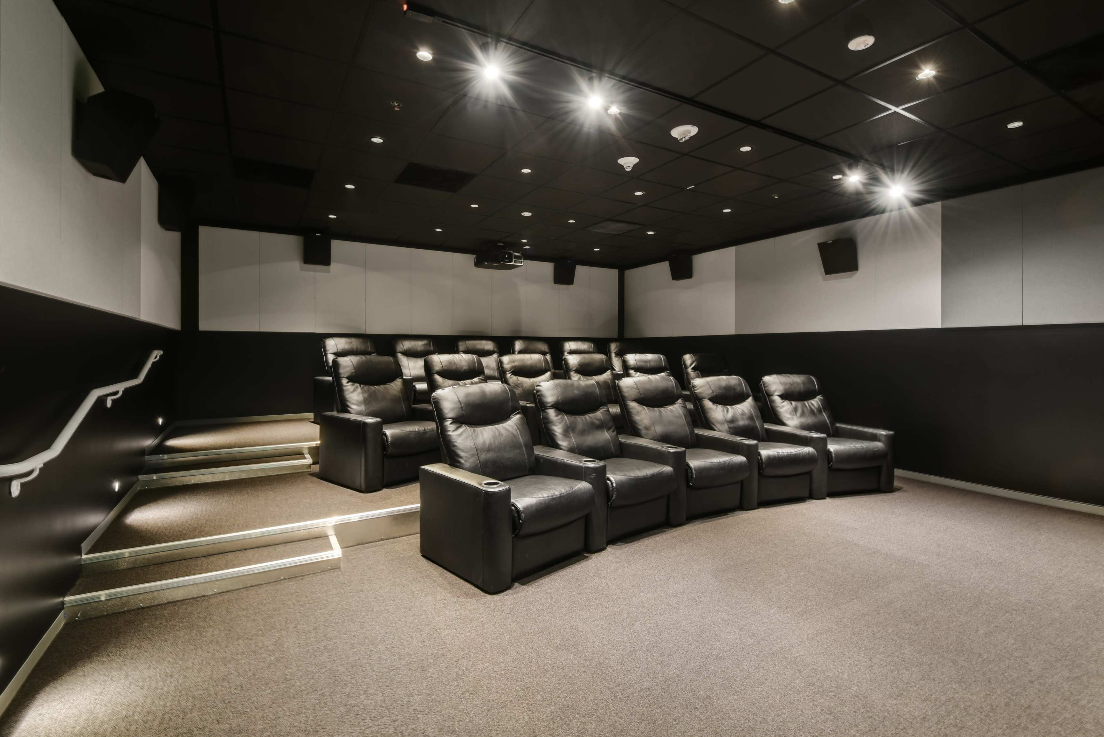 The image shows a small, modern home theater with several black reclining chairs arranged in a semi-circle.
