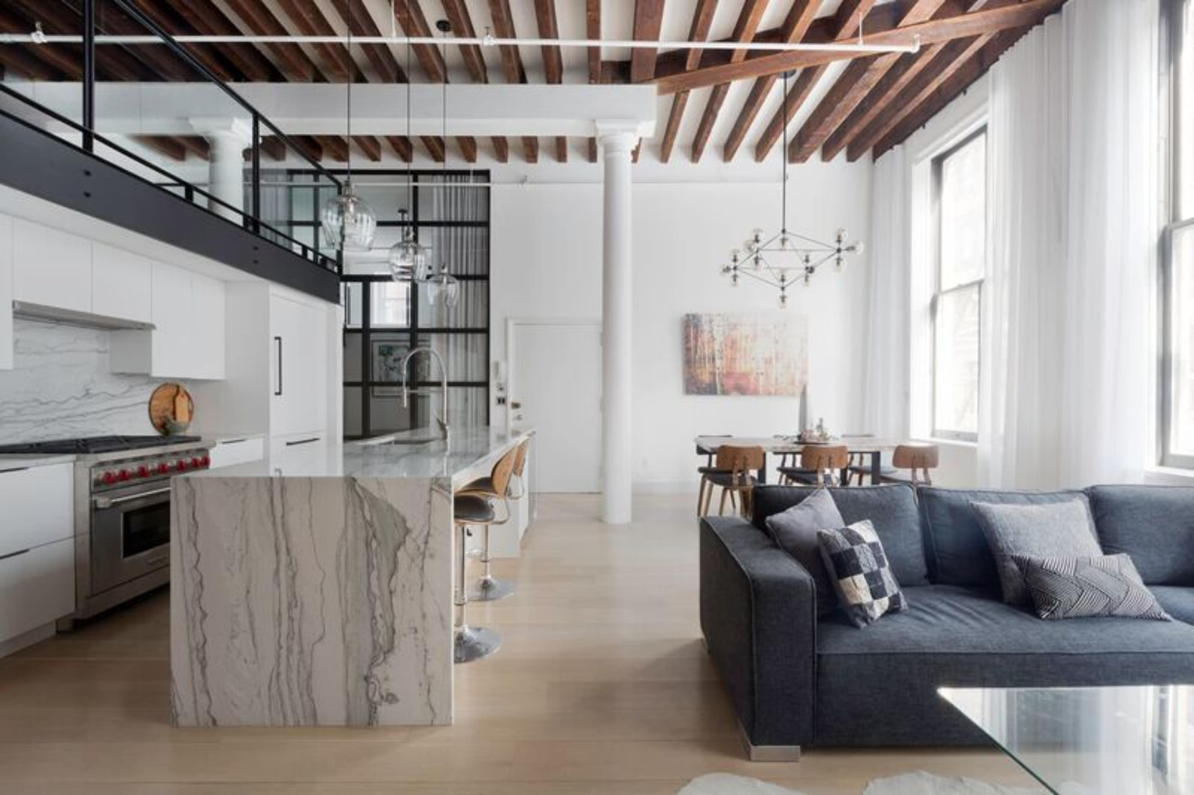 A modern open-concept living space with a kitchen island, dining area, and a seating area featuring a dark sofa.