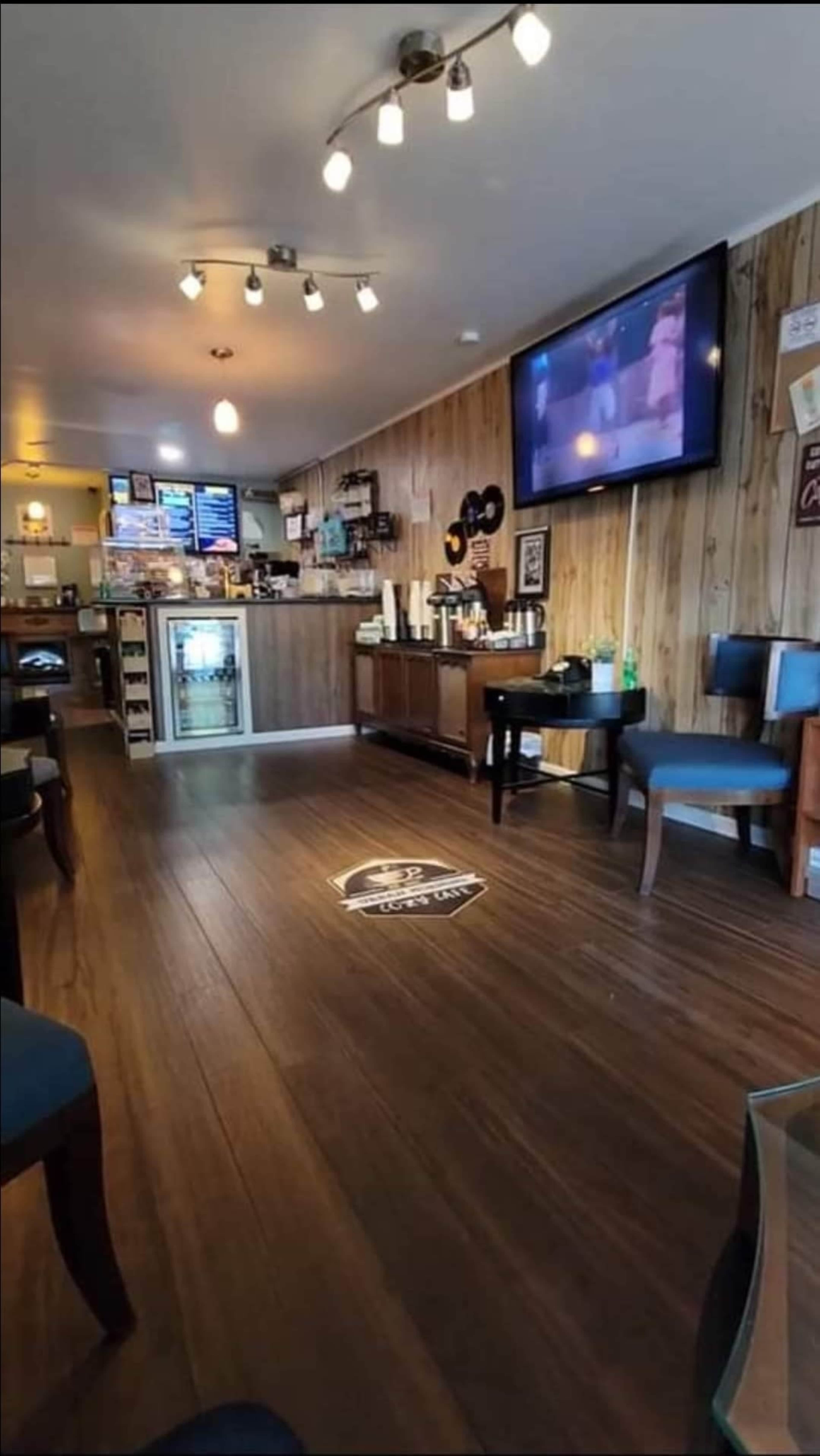 The image shows the interior of a casual café with wooden paneling, a service counter in the back, and a television mounted on the wall.