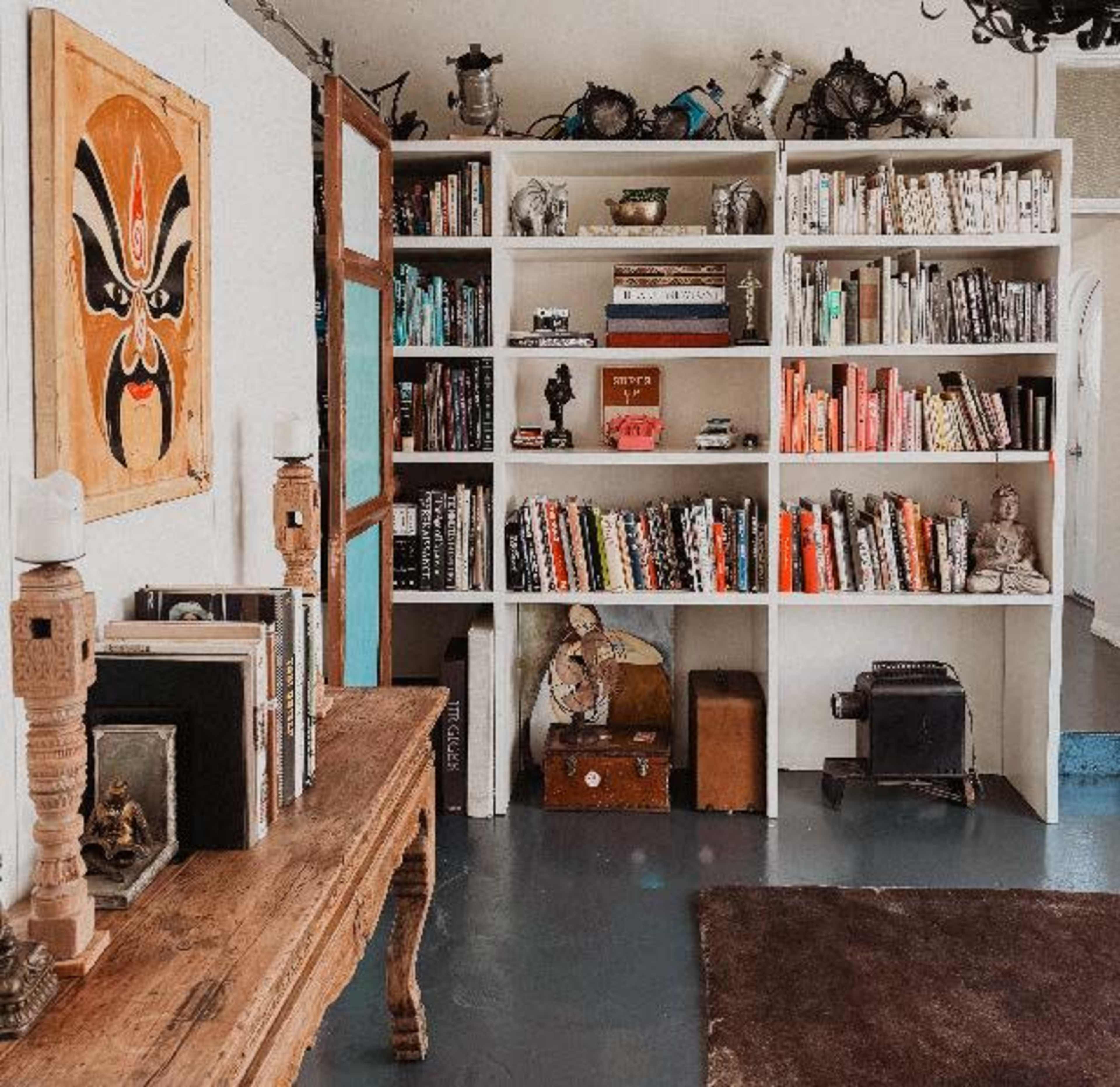 The image shows a bookshelf filled with a variety of books and decorative items, alongside a wooden bench and a dark rug on the floor.