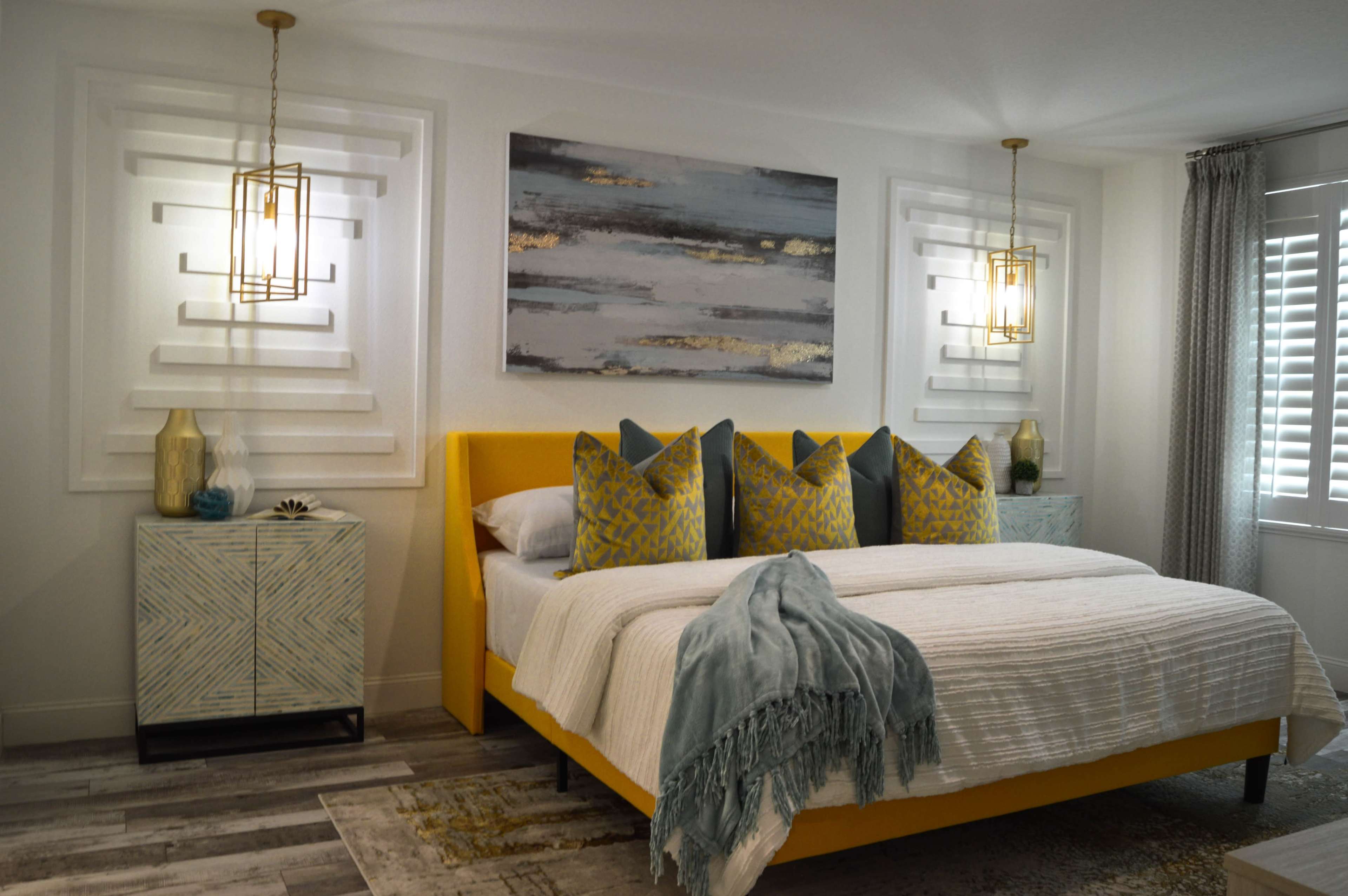 The image shows a bright bedroom featuring a yellow bed with decorative pillows, flanked by nightstands and illuminated by pendant lights.