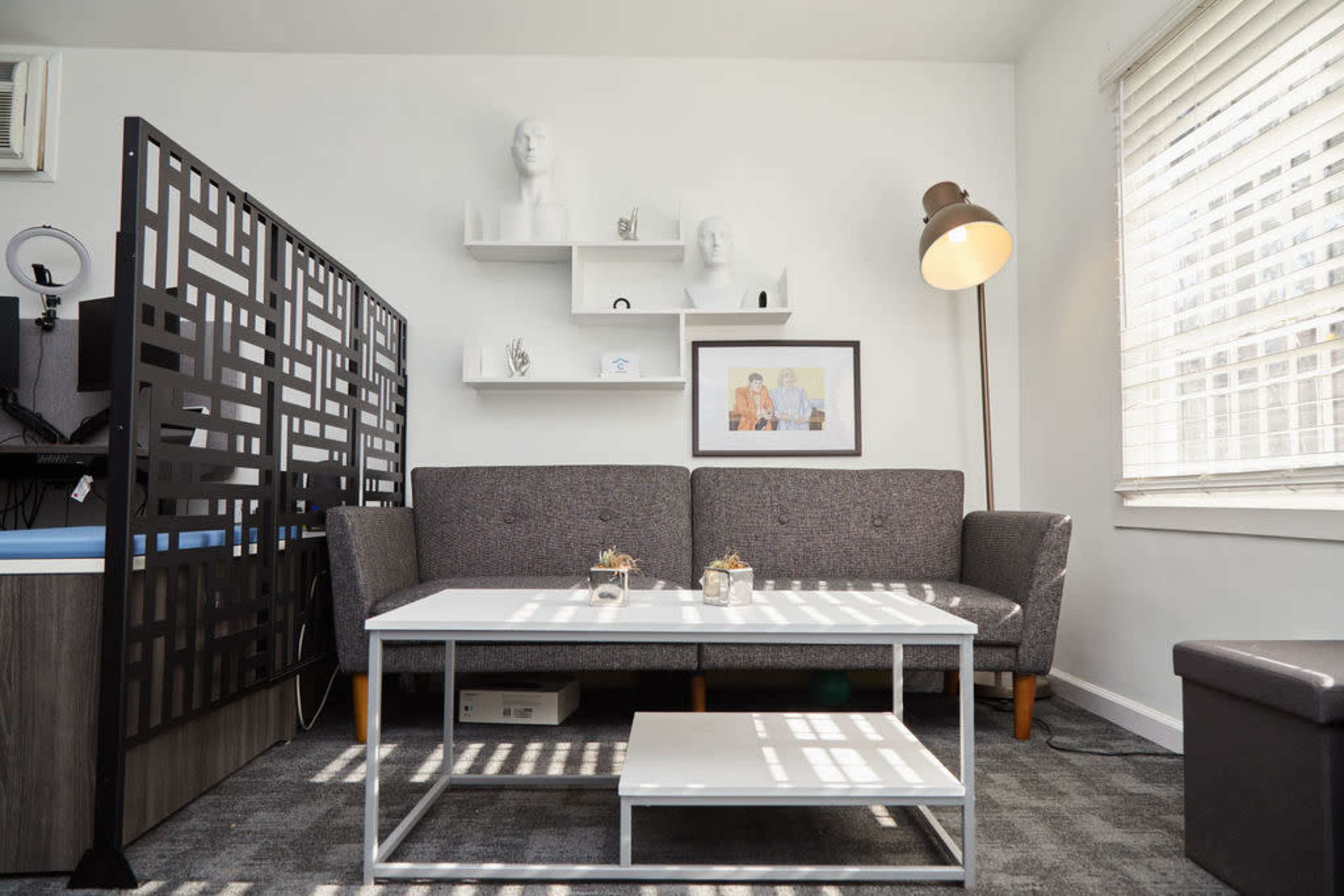 A modern living room with a gray sofa, a coffee table, and decorative shelves featuring sculptures and framed artwork.